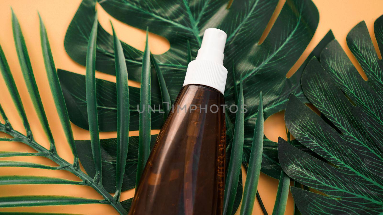 Suntan lotion bottle on soft orange background with tropical leaf. Top view, copy space. Sun protection cosmetic products, summer skin care concept