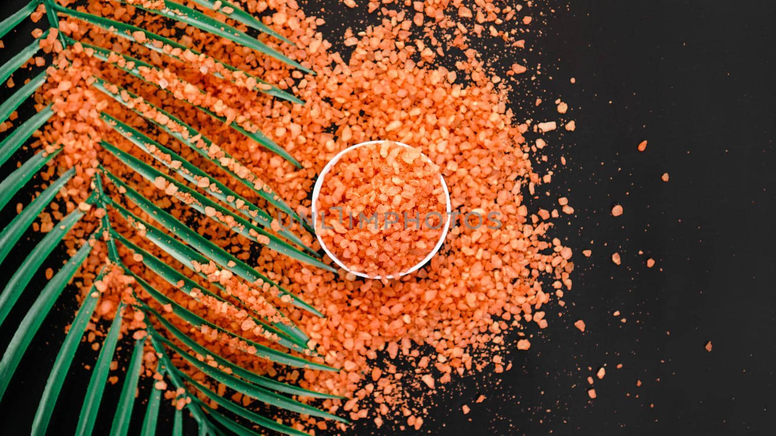 Orange sea salt on a black background. Tropical palm leaves on background. Beauty concept. Spa background with a space for a text