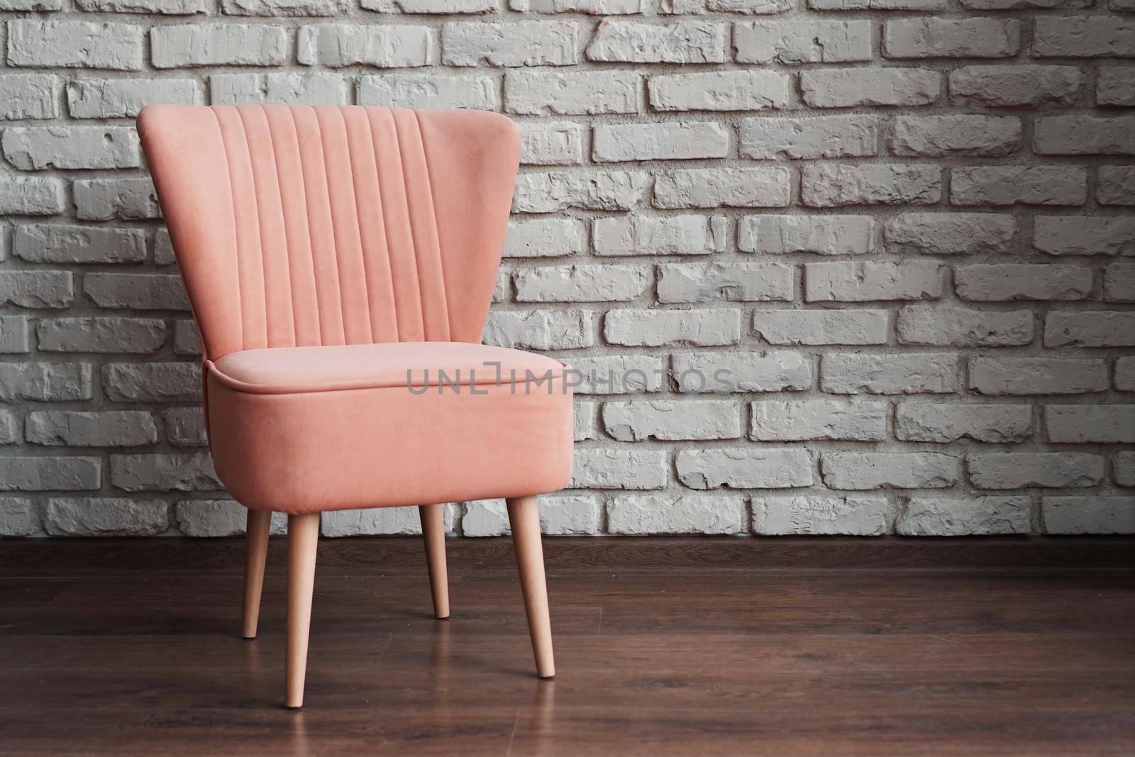 Modern pink soft chair against white brick wall and brown laminate in photo studio