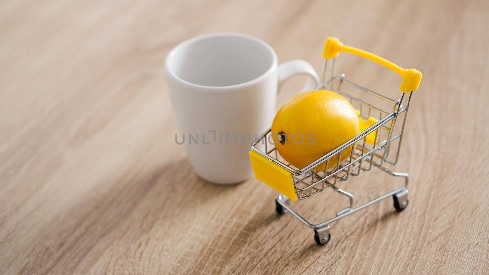 Lemon in a small shopping cart on the kitchen table. Nearby is a white mug of tea. Light and modern kitchen background.