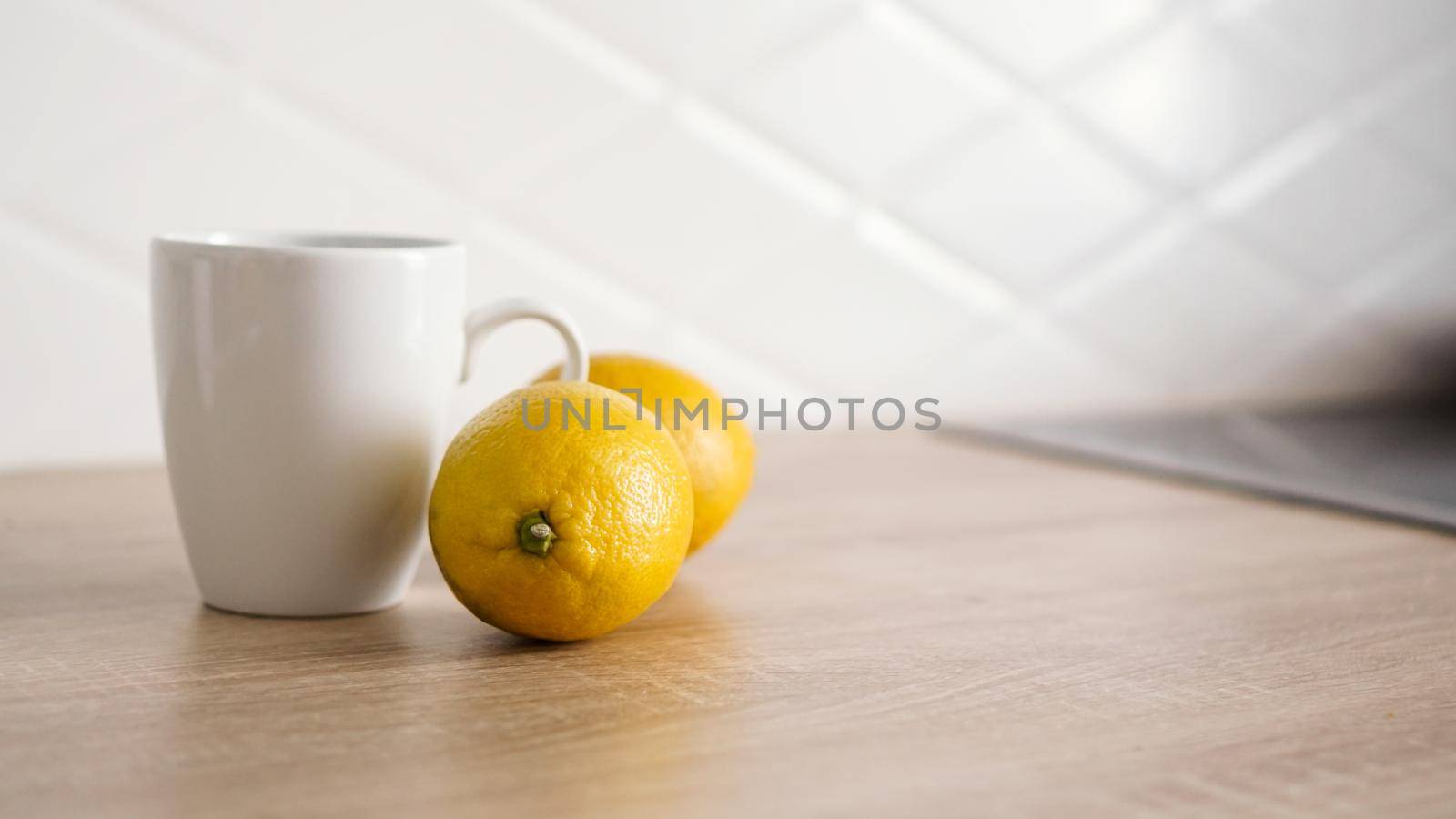 Two lemons on the kitchen table near a white mug of tea. Morning concept