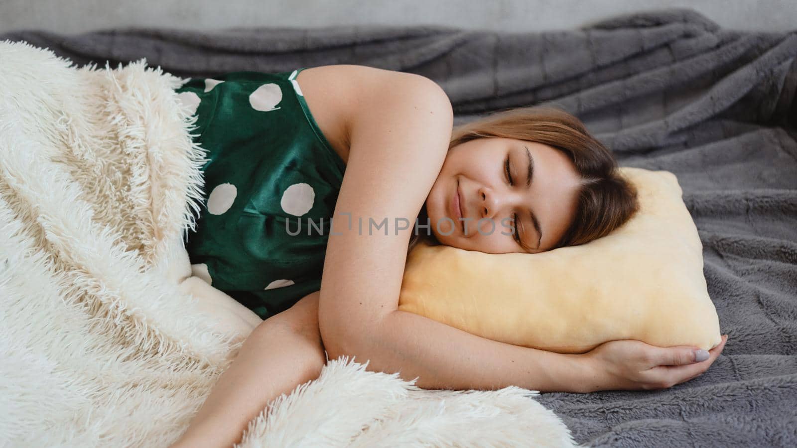 Beautiful young girl in a green nightie sleeps on a yellow pillow on a sofa under a white blanket