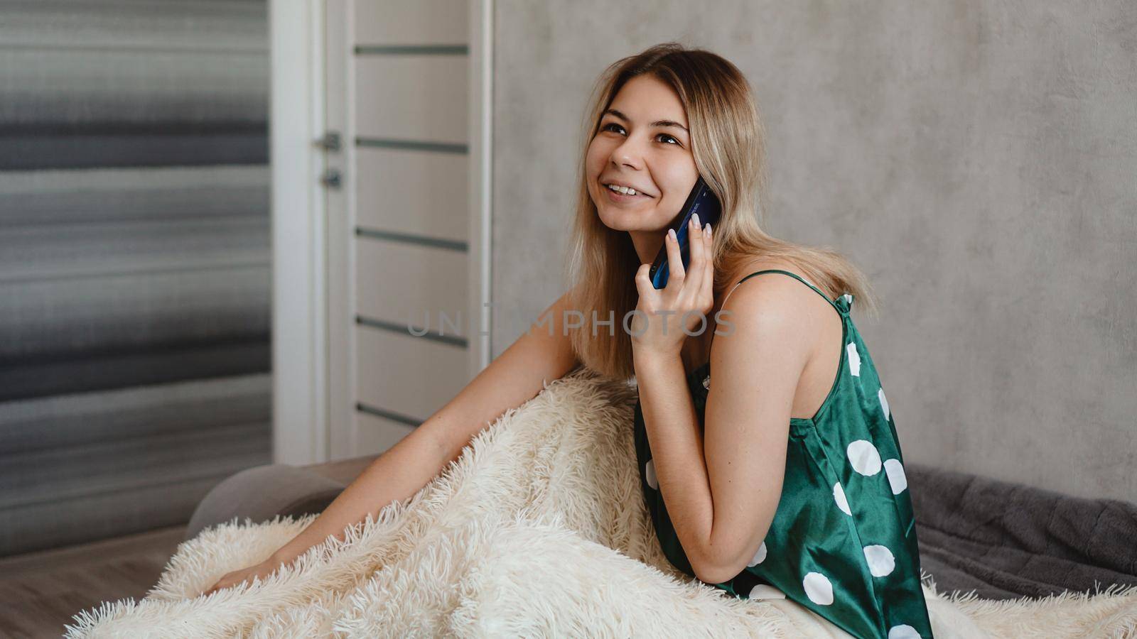 Attractive relaxed young woman sitting in bed and talking on smartphone