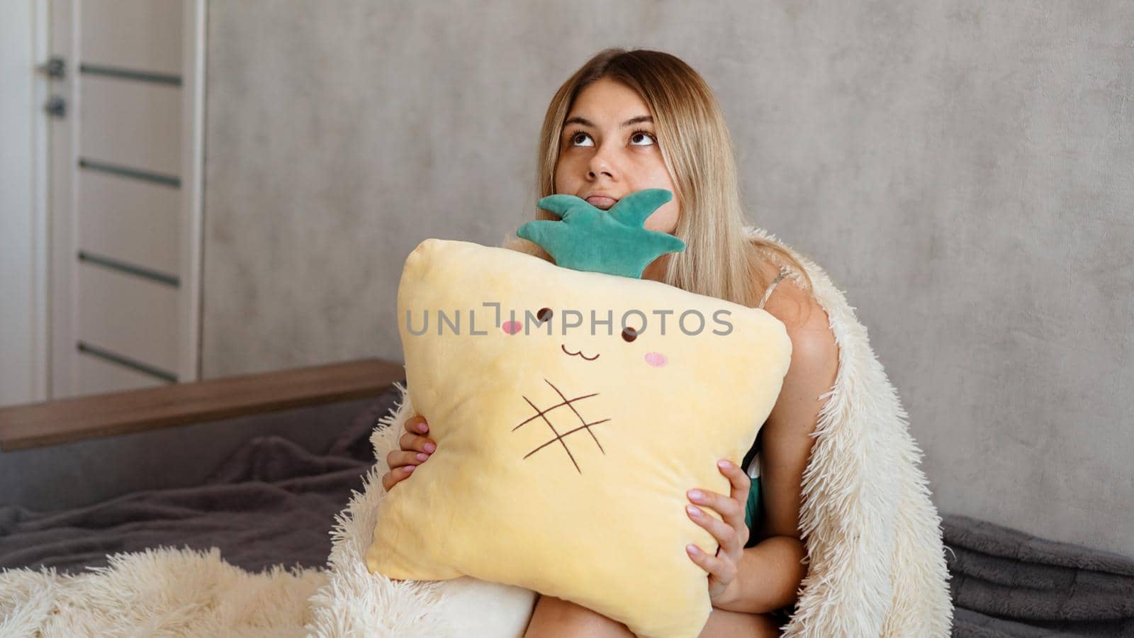 Young woman sitting on sofa and thinking. Beautiful girl holding cushion and looking serious or sad