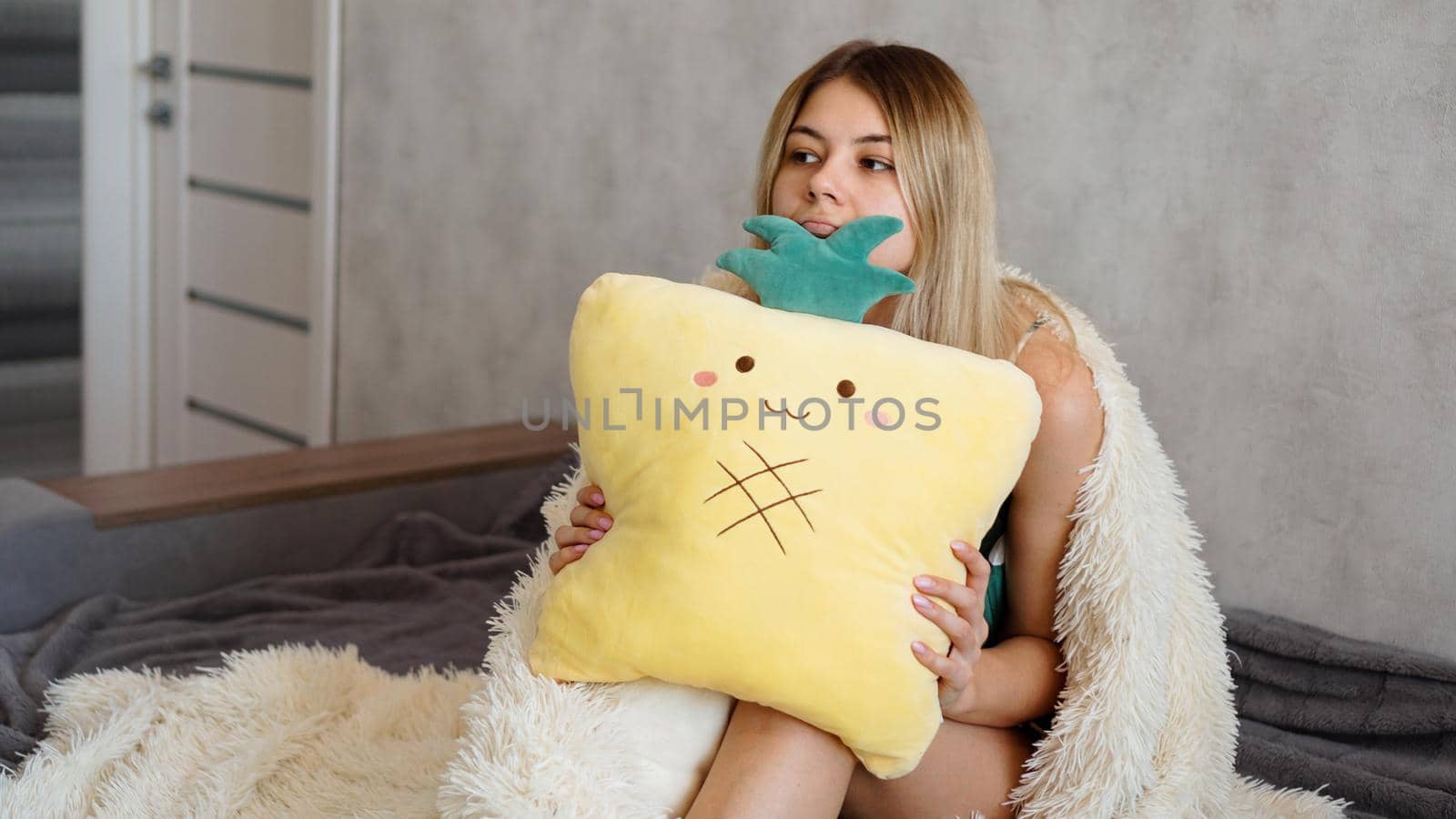 Young woman sitting on sofa and thinking. Beautiful girl holding cushion and looking serious or sad