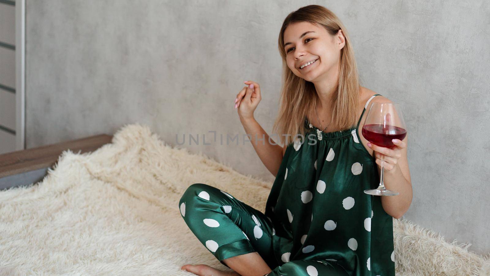 Girl in green pajamas in bed with a glass of red wine. Morning wine in bed