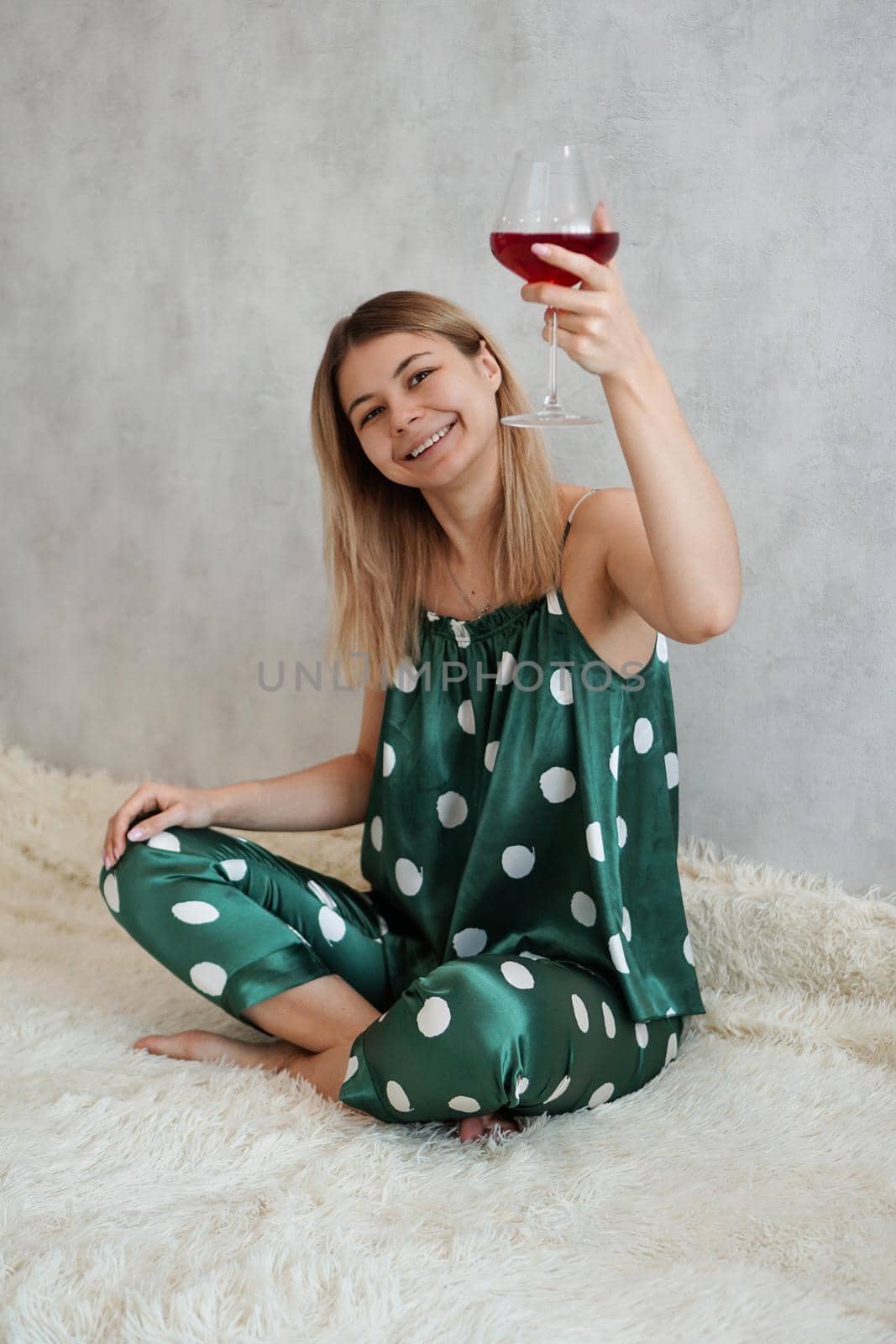 Girl in green pajamas in bed with a glass of red wine. Morning wine in bed. Vertical photo