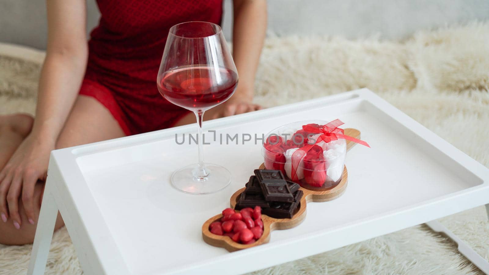 Breakfast for girlfriend. Valentines Day Morning. Wine and sweets on a white tray. Breakfast in bed. Girl in a red peignoir on the background