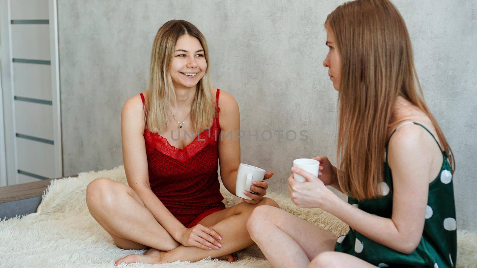 Portrait two funny girls in pajamas having fun. They chat and drink tea by natali_brill