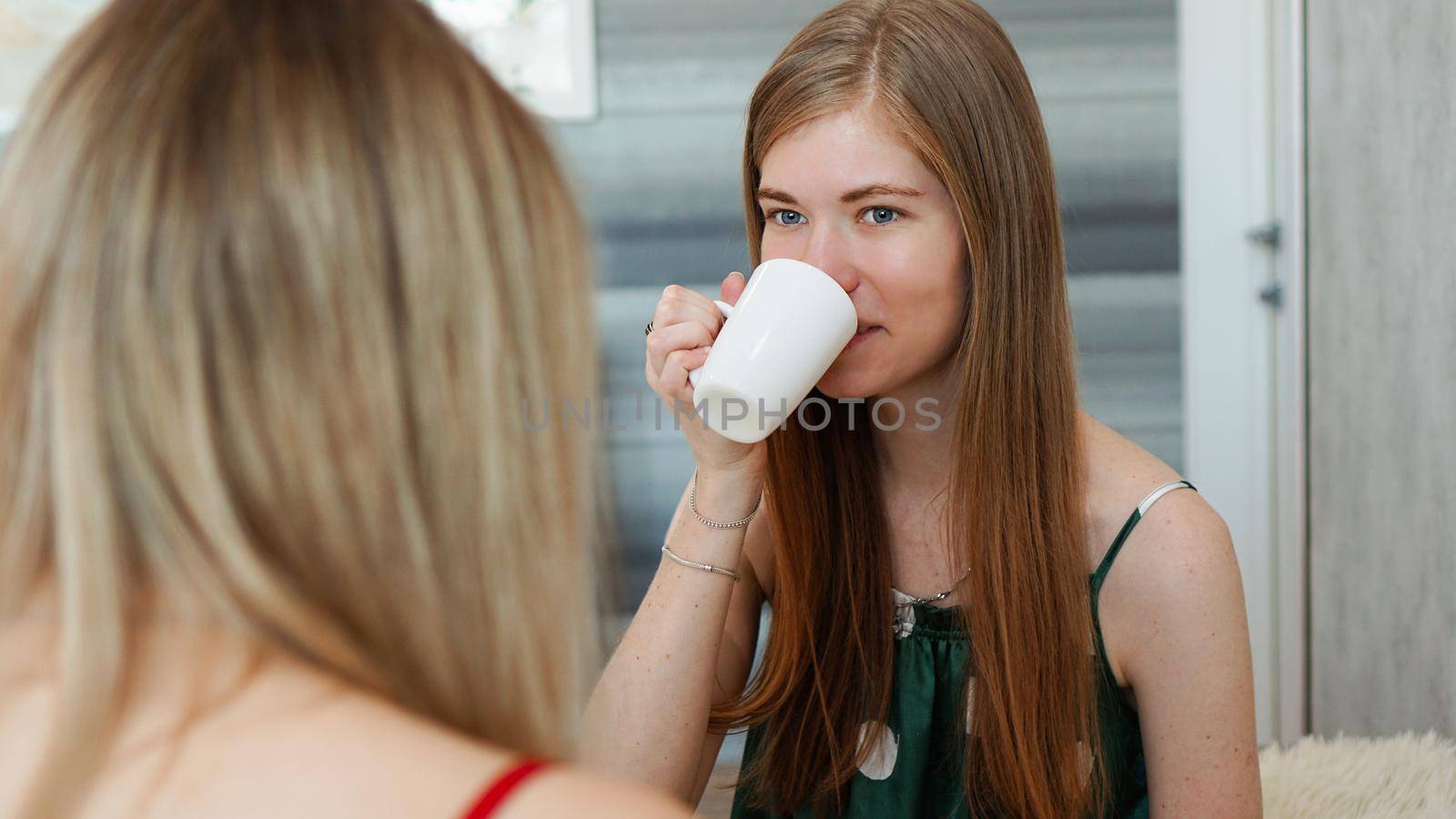 Portrait two funny girls in pajamas having fun. They chat and drink tea by natali_brill