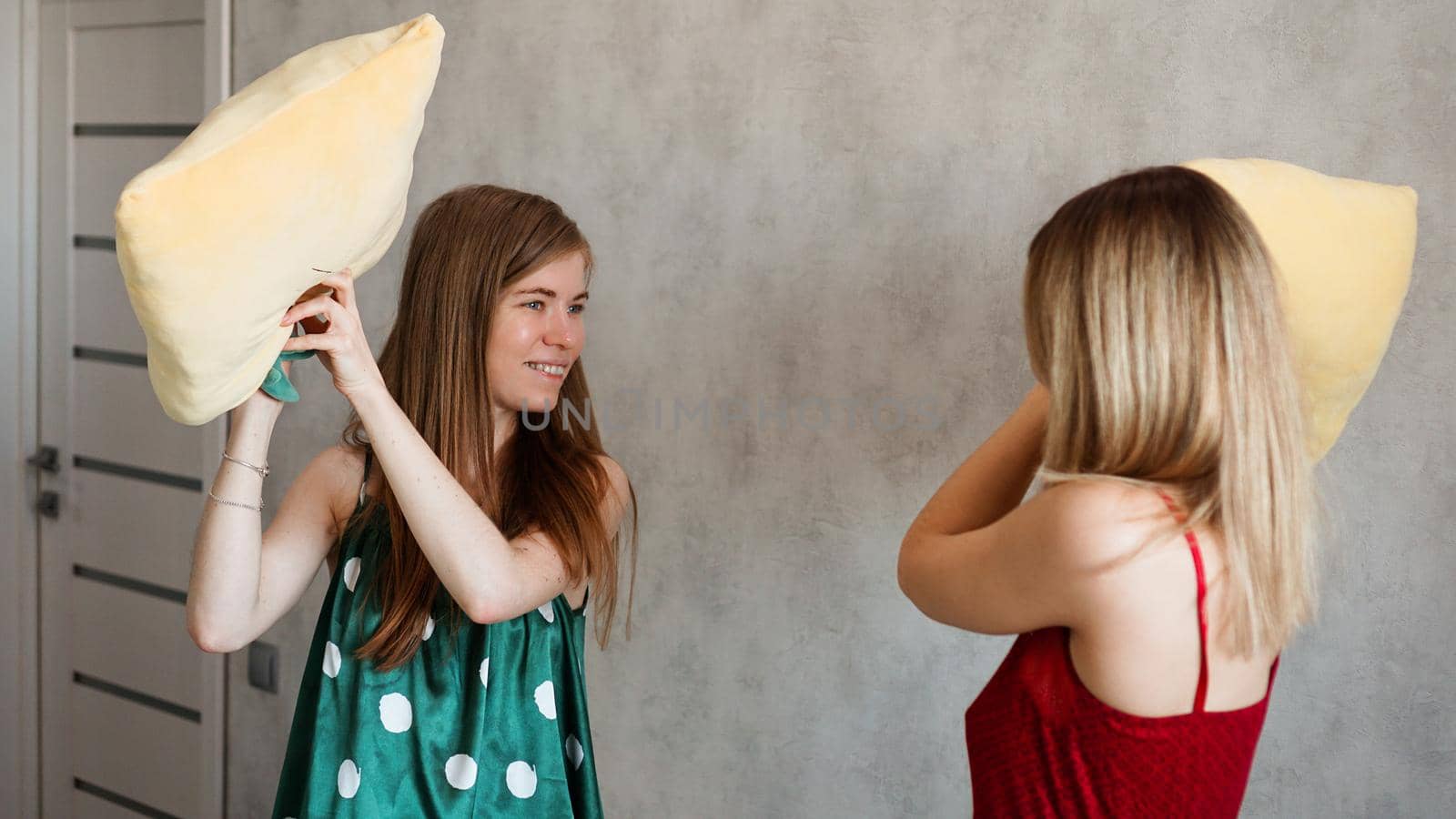 Two girl friends pillow fight in room at a pajama party