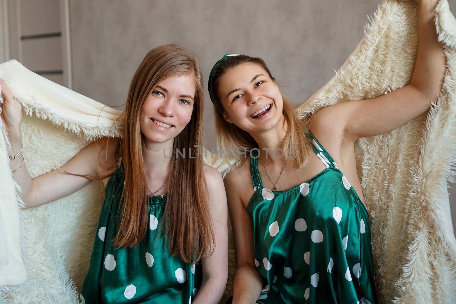 Two laughing young woman having fun when hiding under white blanket by natali_brill