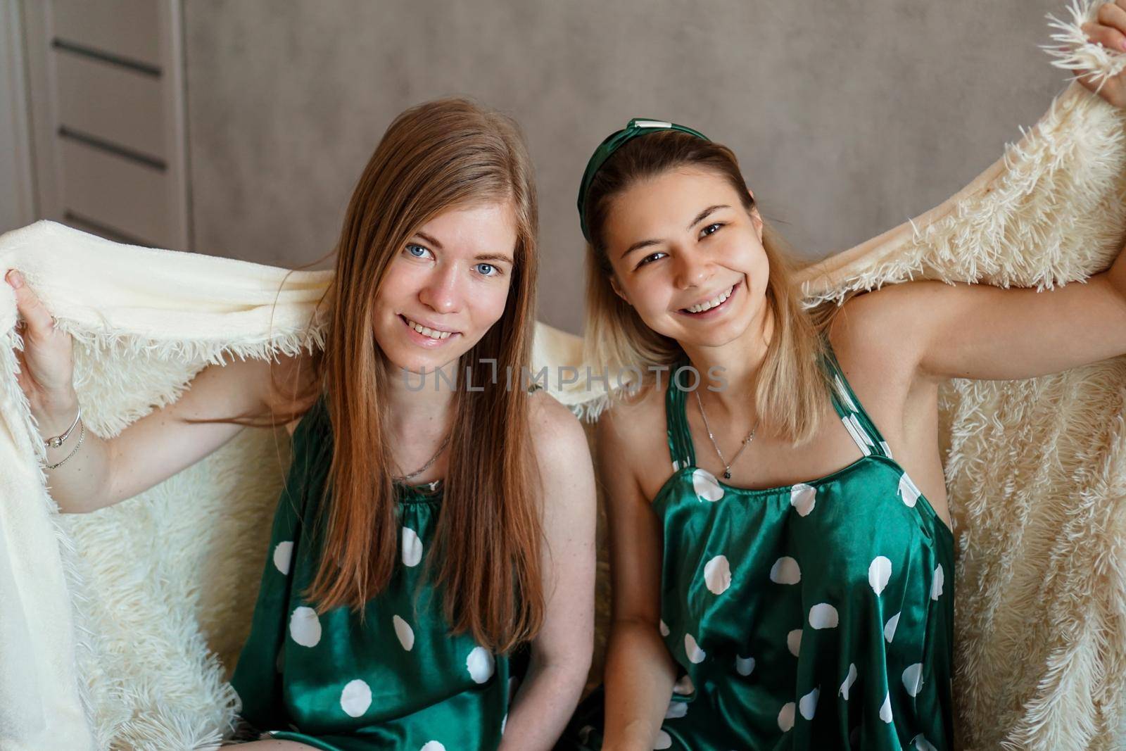 Two laughing young woman having fun when hiding under white blanket by natali_brill