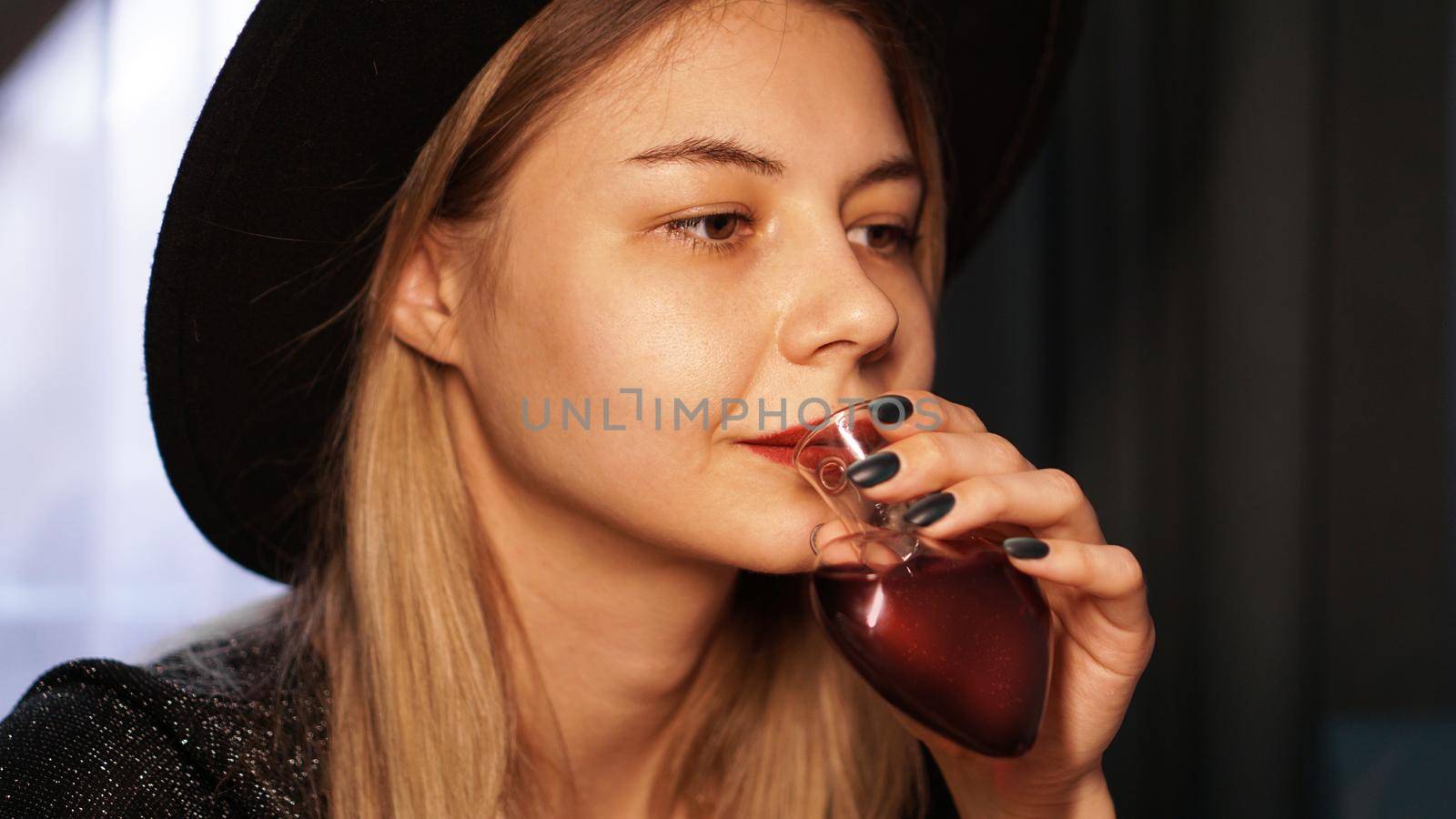 Beautiful young woman drinking love potion from a bottle in the shape of a heart