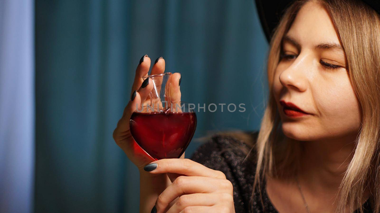Cropped image of woman holding heart shaped glass jar of love potion. Beautiful young woman in a witch hat