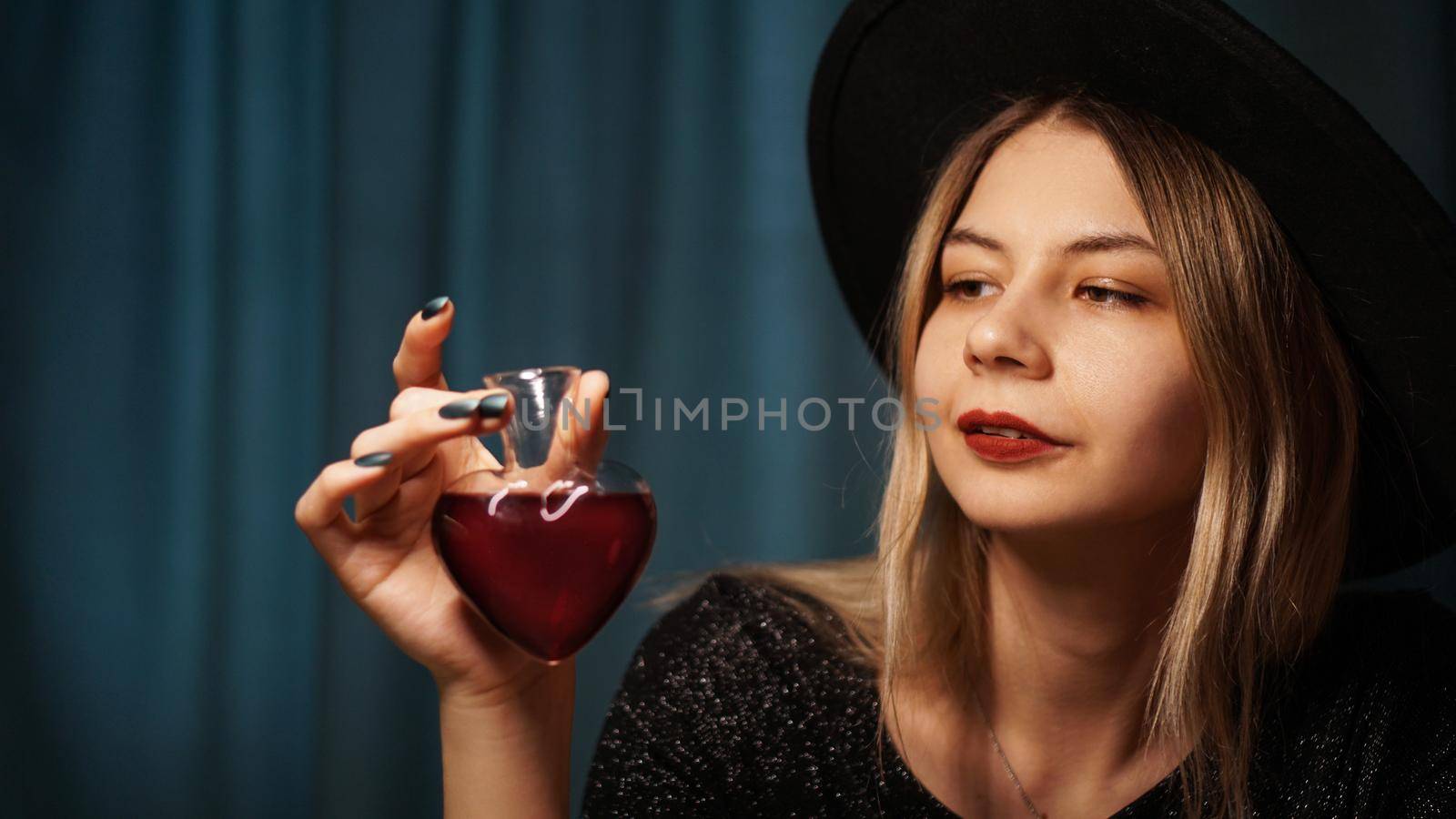 Cropped image of woman holding heart shaped glass jar of love potion. Beautiful young woman in a witch hat