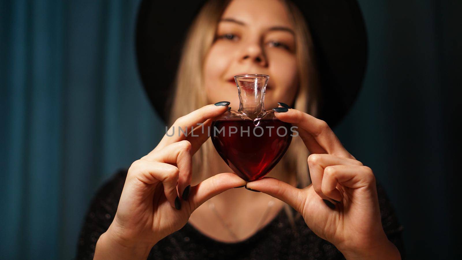 Cropped image of woman holding heart shaped glass jar of love potion. Beautiful young woman in a witch hat