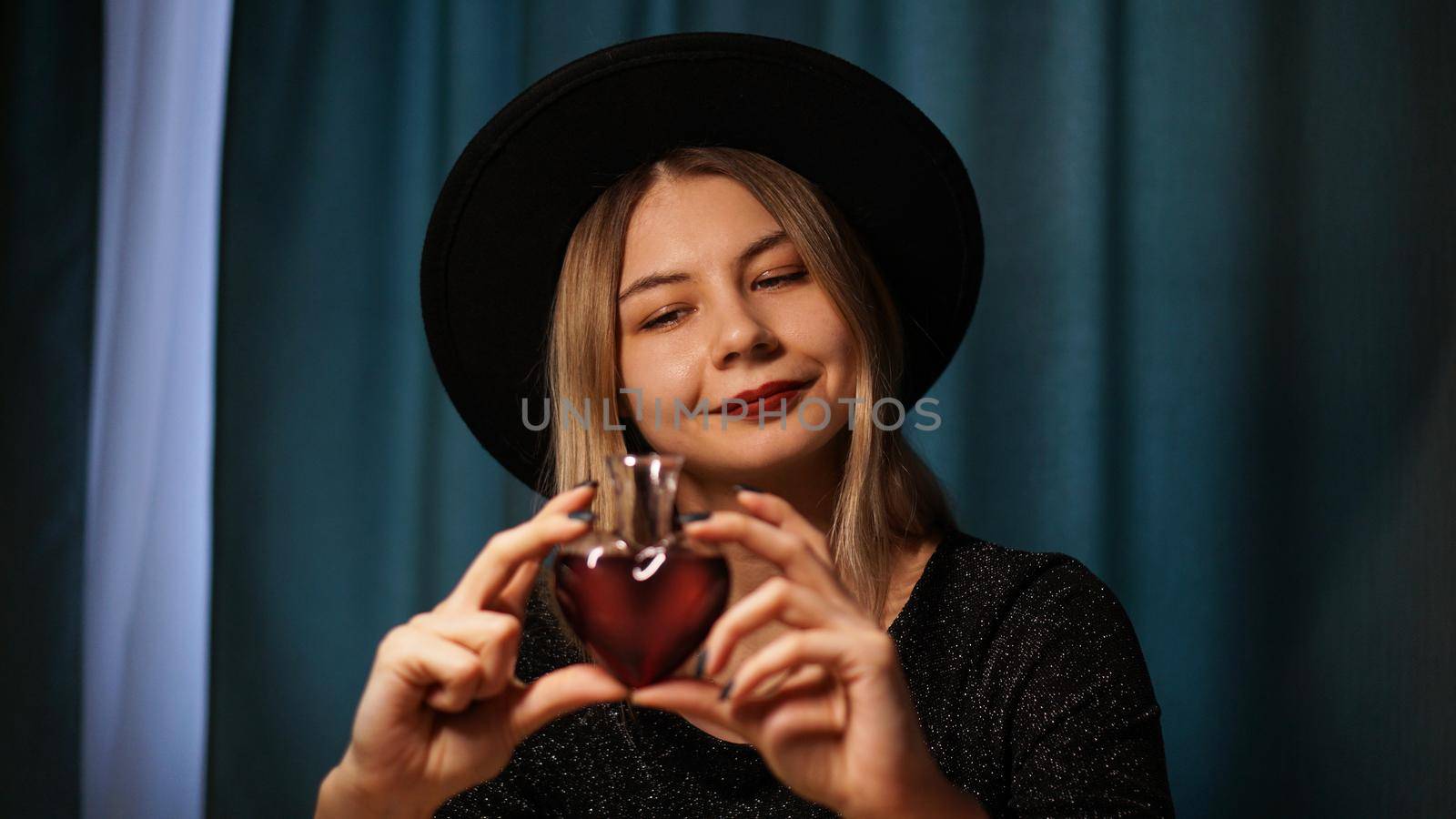 Cropped image of woman holding heart shaped glass jar of love potion. Beautiful young woman in a witch hat