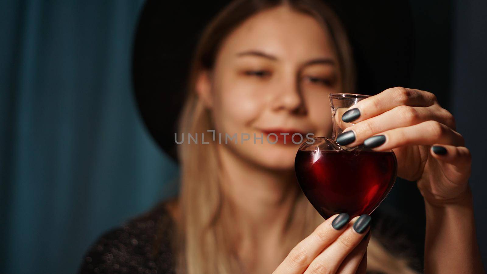 Cropped image of woman holding heart shaped glass jar of love potion. Beautiful young woman in a witch hat. Focus on Potion or Poison Vial