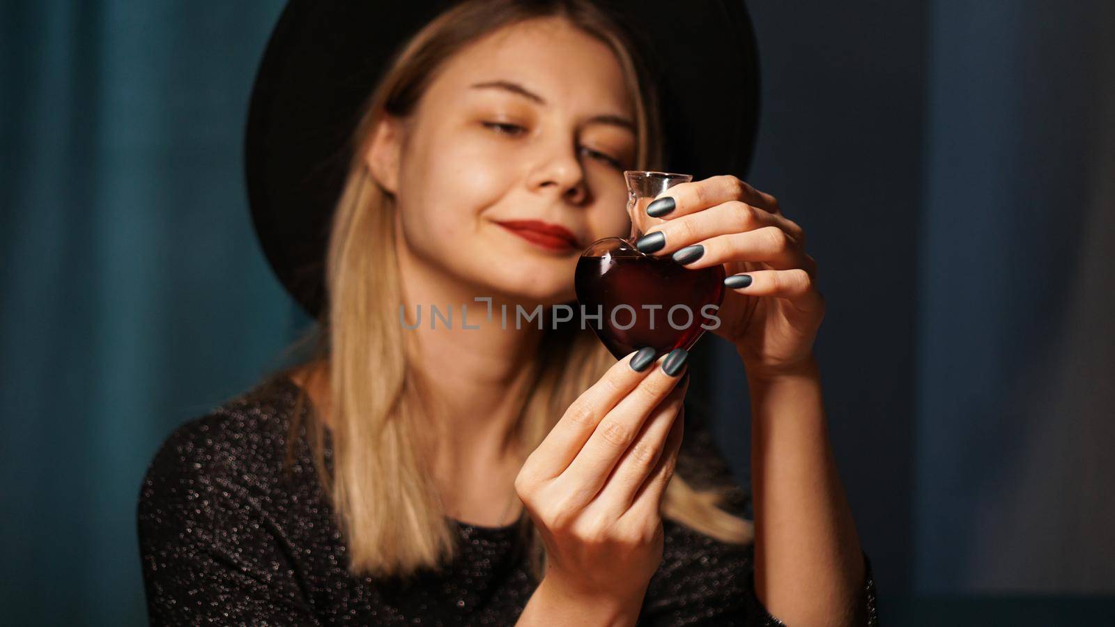 Cropped image of woman holding heart shaped glass jar of love potion. Beautiful young woman in a witch hat. Focus on Potion or Poison Vial