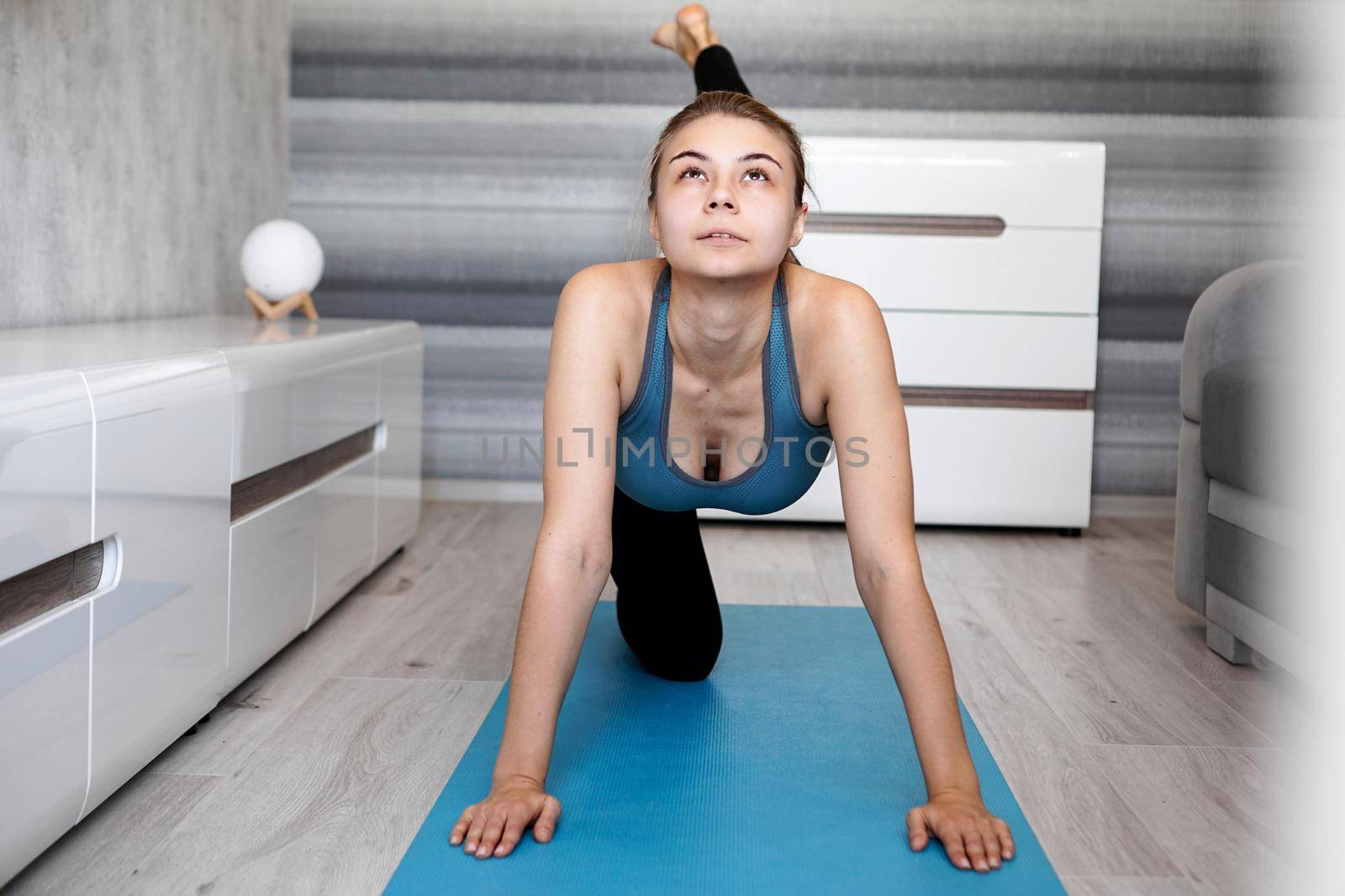 Sport, training and lifestyle concept - woman stretching leg on blue yoga mat at home in the living room