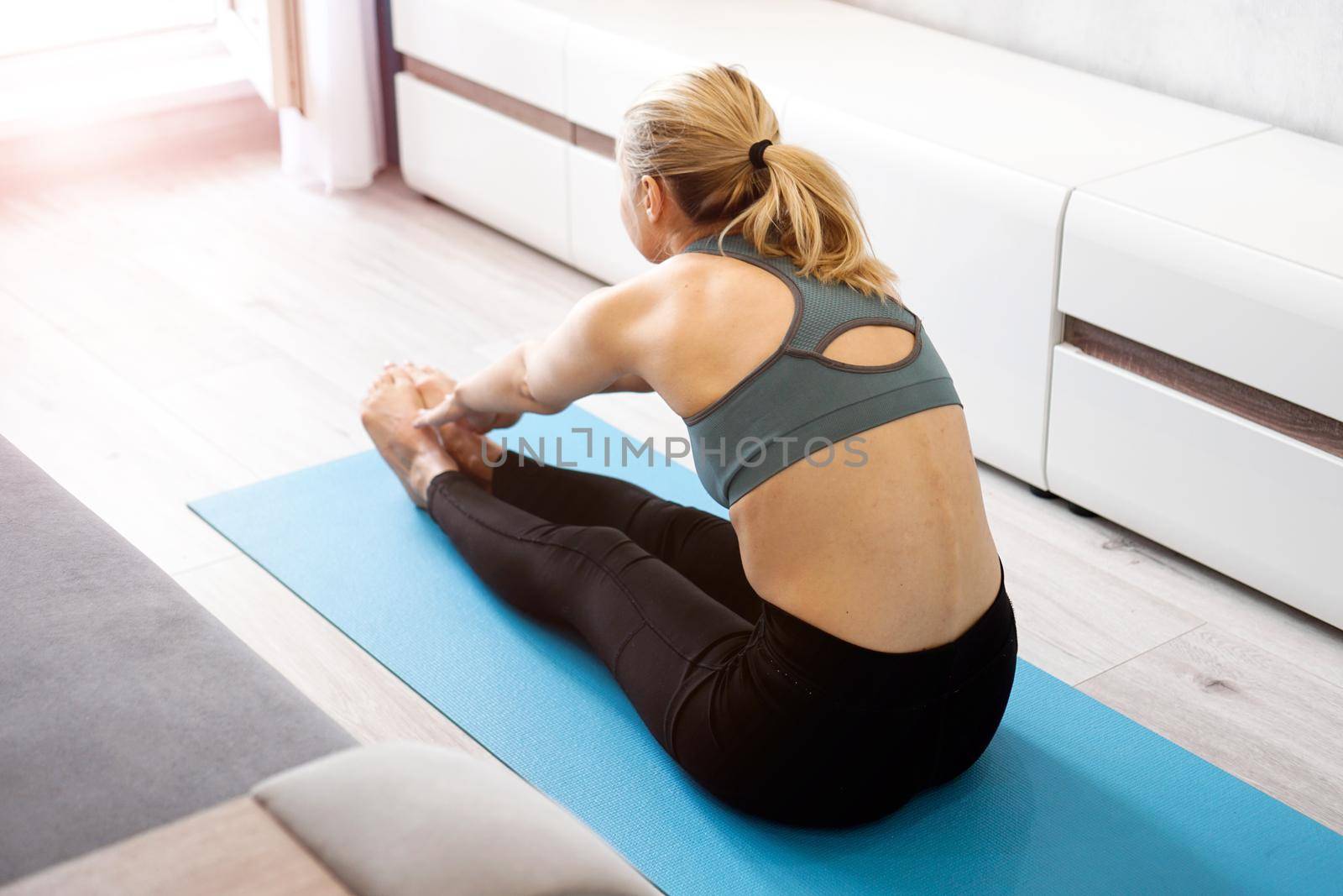 Fitness woman stretching legs sitting on the floor at home