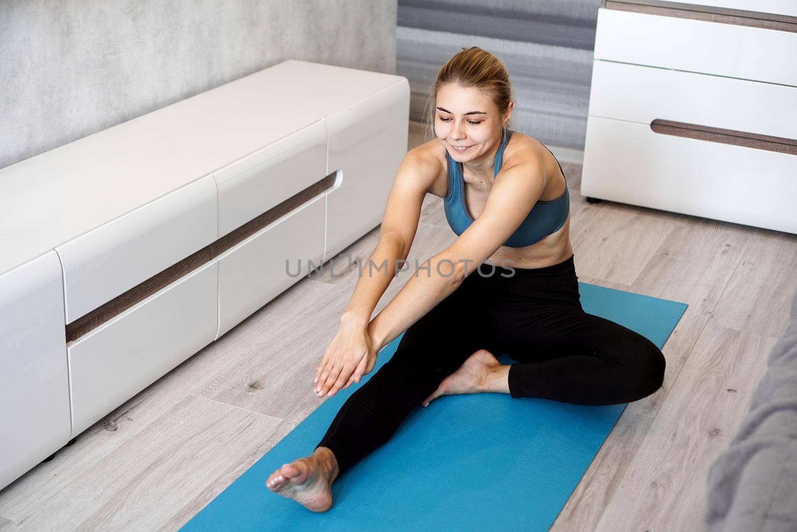 Sport, training and lifestyle concept - woman stretching leg on mat at home by natali_brill