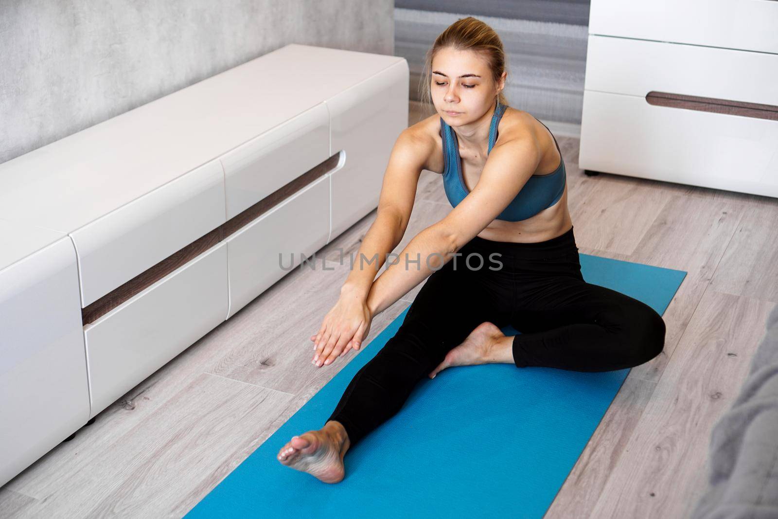 Sport, training and lifestyle concept - woman stretching leg on blue yoga mat at home in the living room