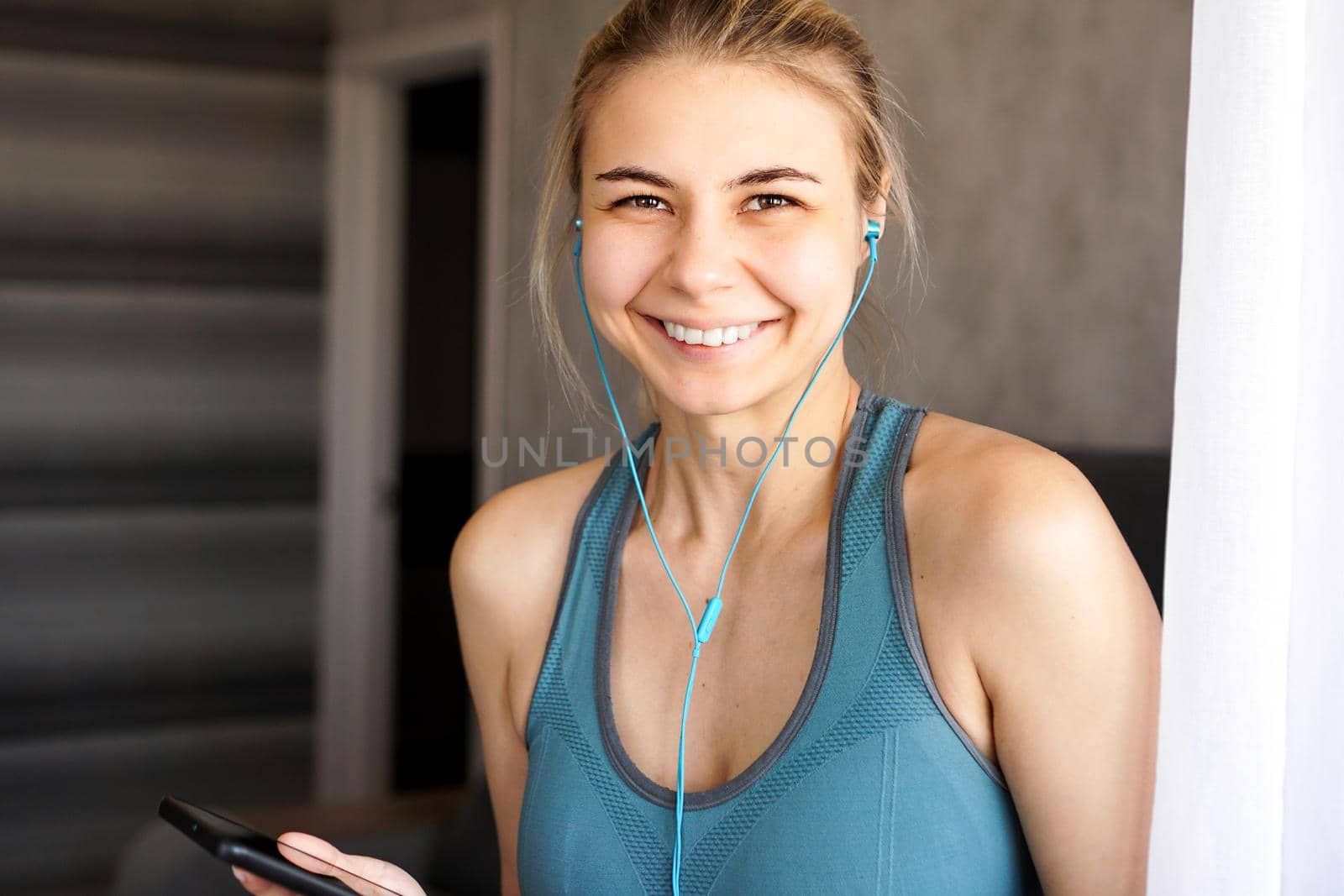Young pretty sporty girl at home listens to music on headphones from smartphone
