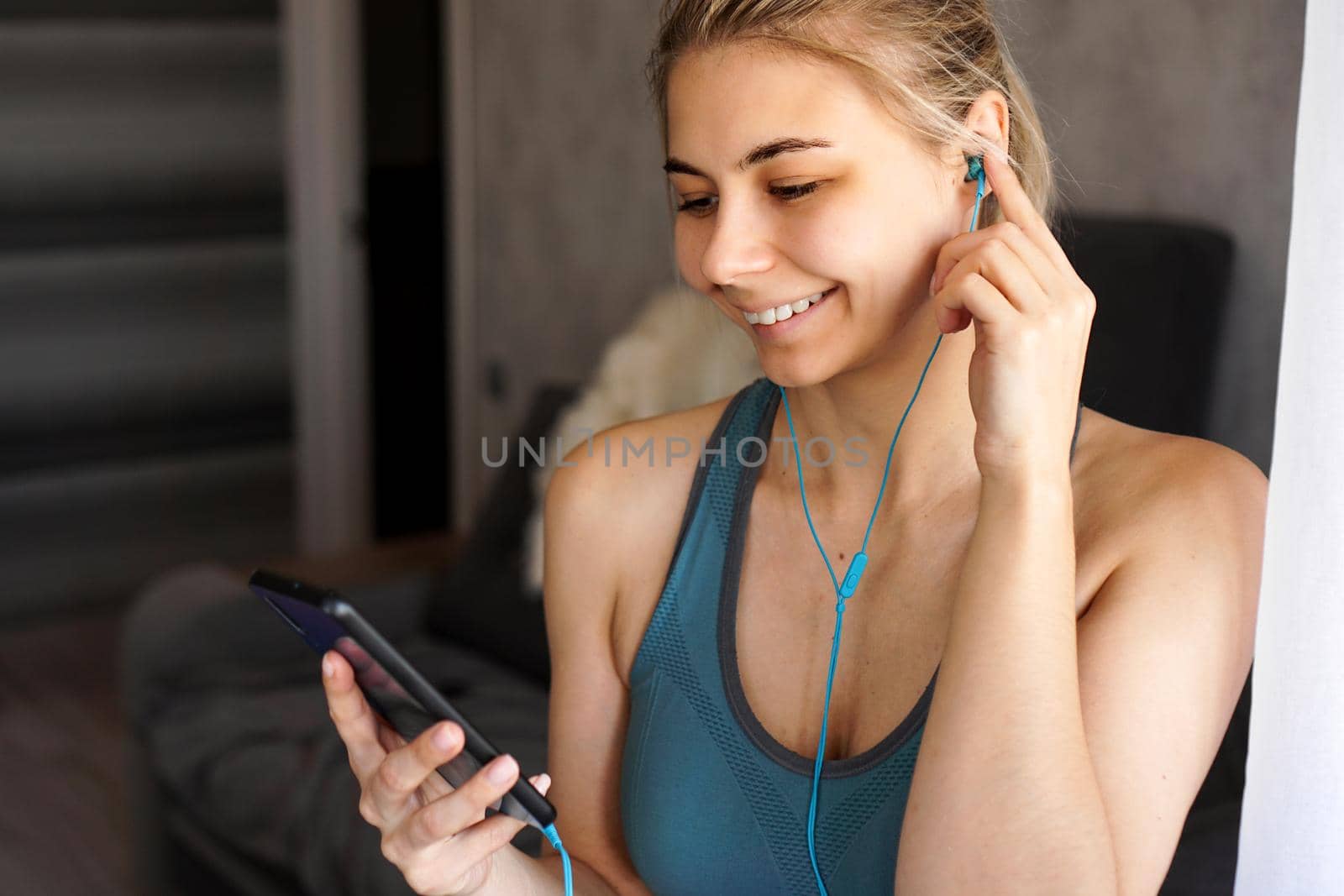 Young pretty sporty girl at home listens to music on headphones from smartphone