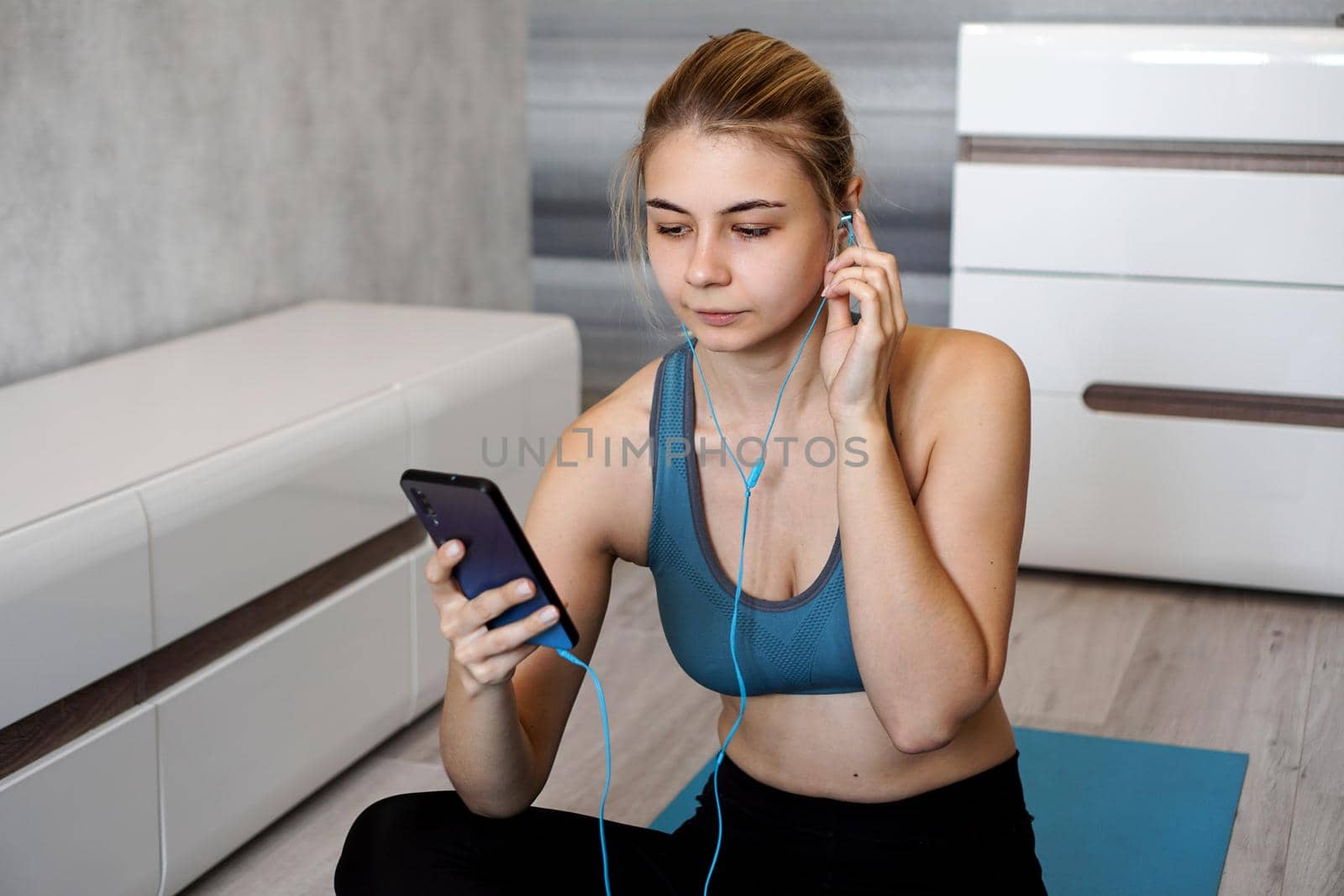 Take sport and add music. Female athlete with earphones enjoying the music playing and touching a screen of her phone while sitting on the floor.