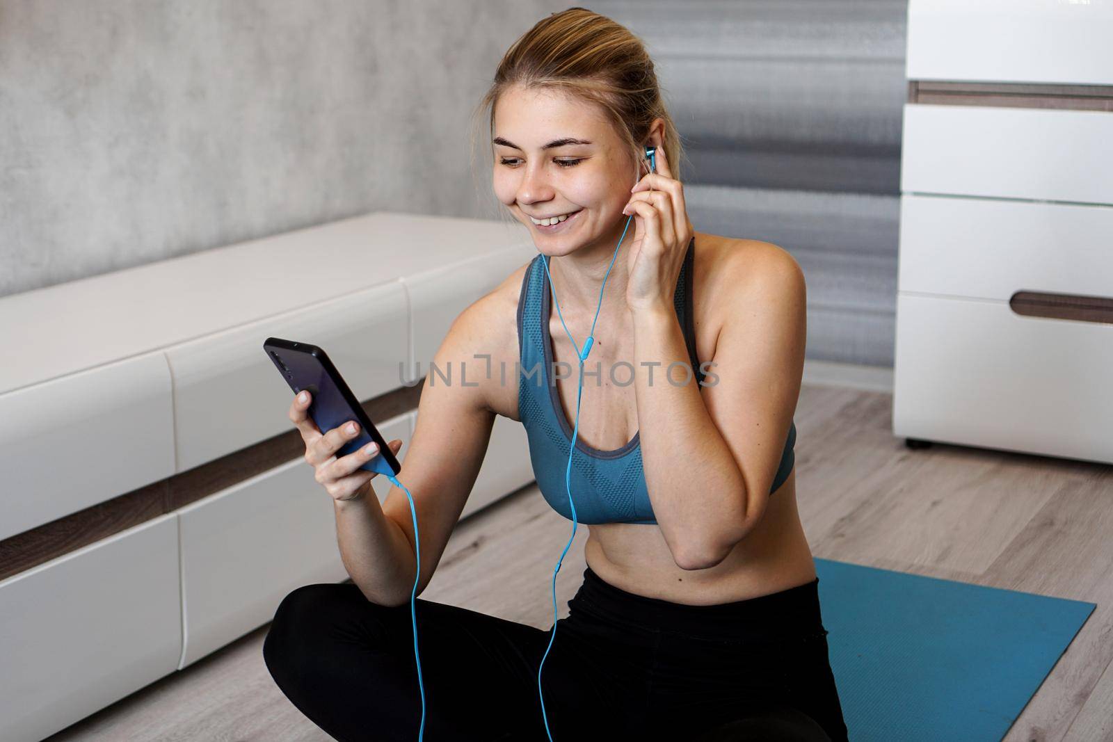 Sport woman with earphones enjoying the music playing while sitting on the floor by natali_brill