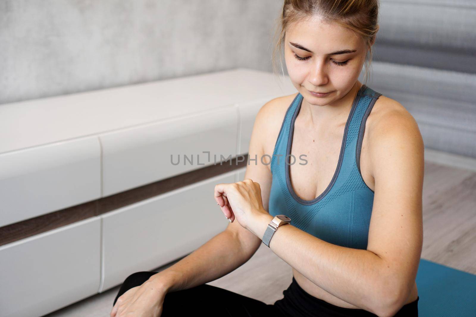 Portrait of young woman checking digital fitness tracker during self-training at home