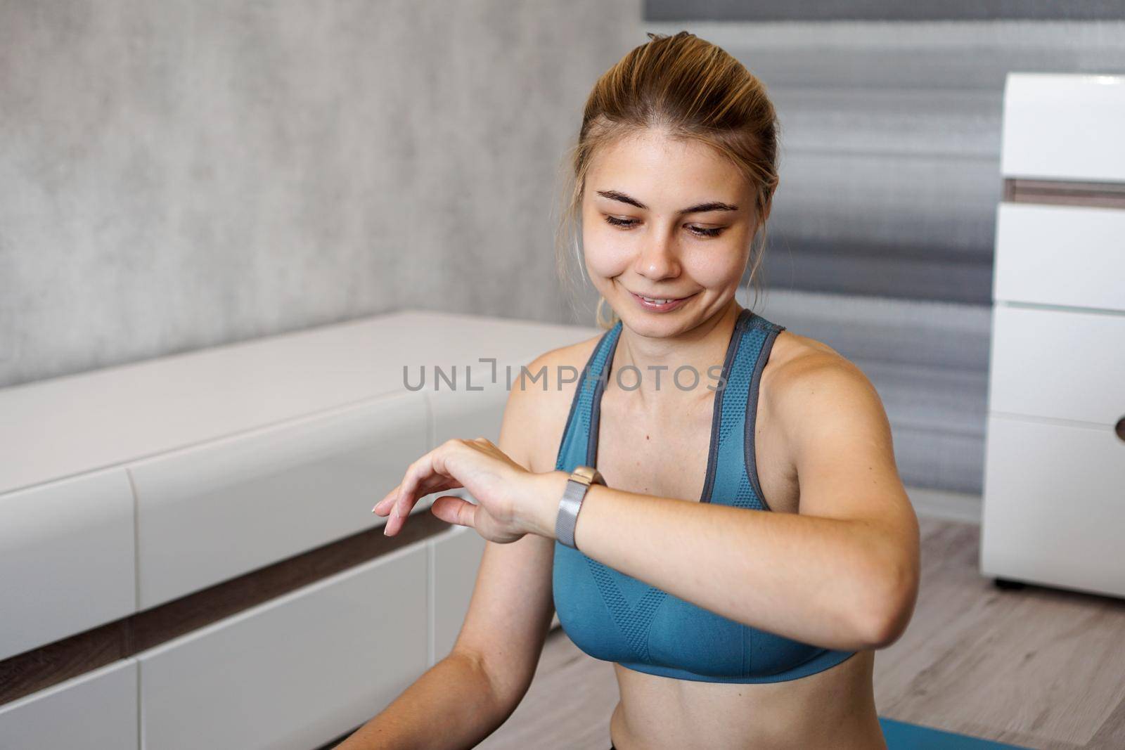 Portrait of young woman checking digital fitness tracker during self-training at home and smiling