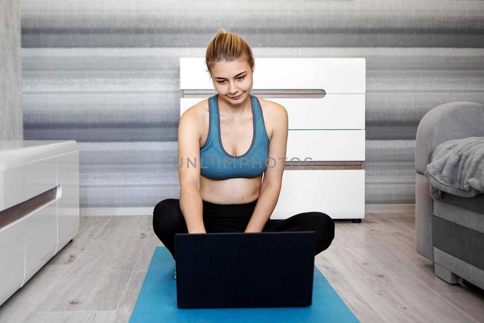 Girl training at home and watching videos on laptop before starting, training in living room