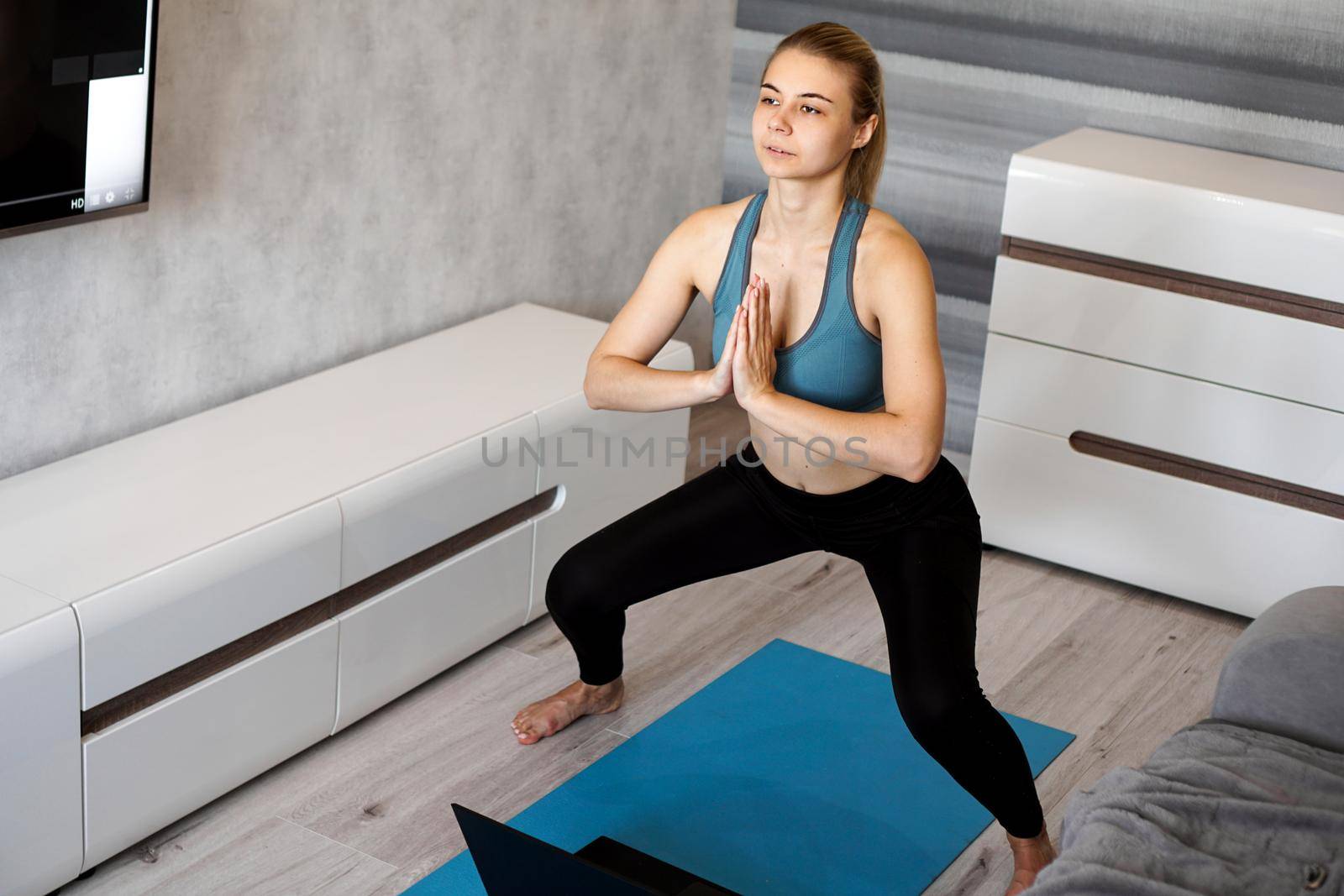Young woman exercising and doing squats. Fitness girl exercising watching on line videos on laptop in the living room at home