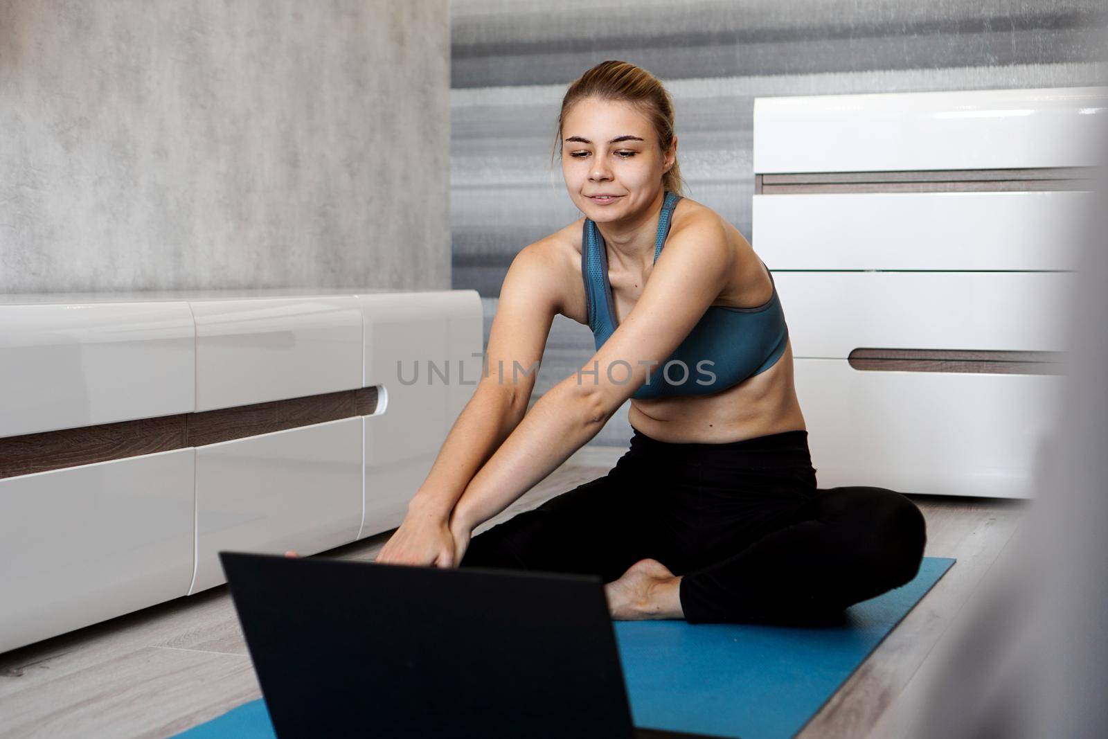 Pretty young woman in sportswear watching online video on laptop and doing exercises at home. Distant training with personal trainer, online education
