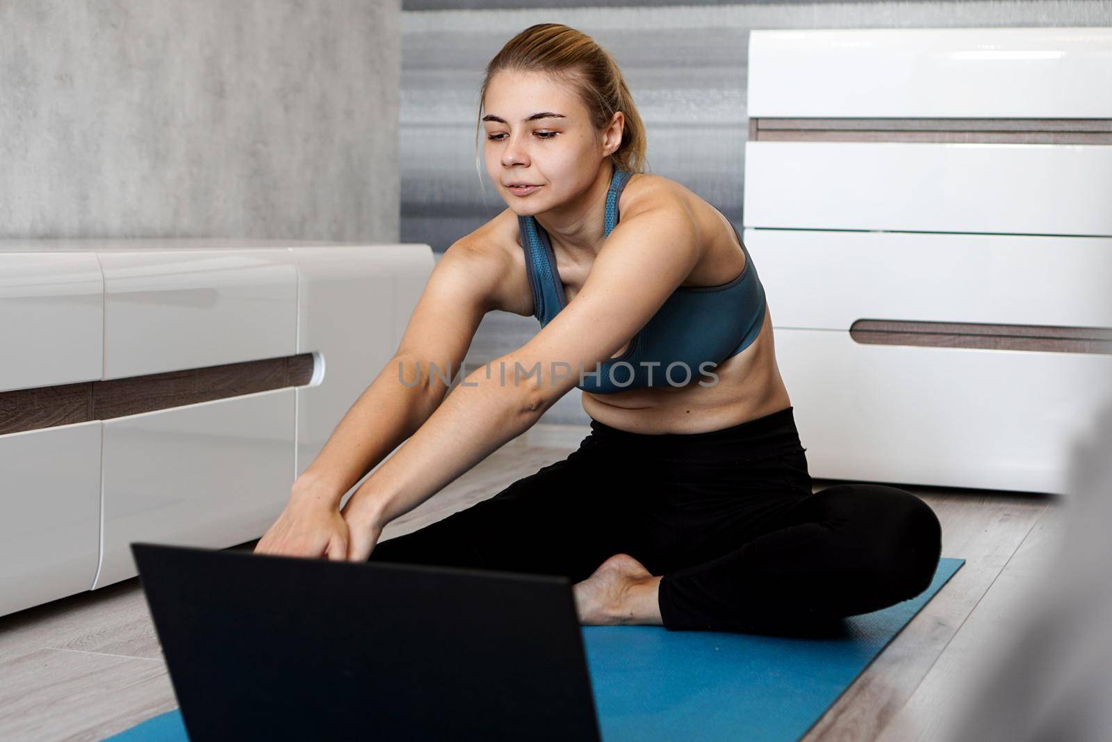 Woman in sportswear watching online video on laptop and doing exercises at home by natali_brill