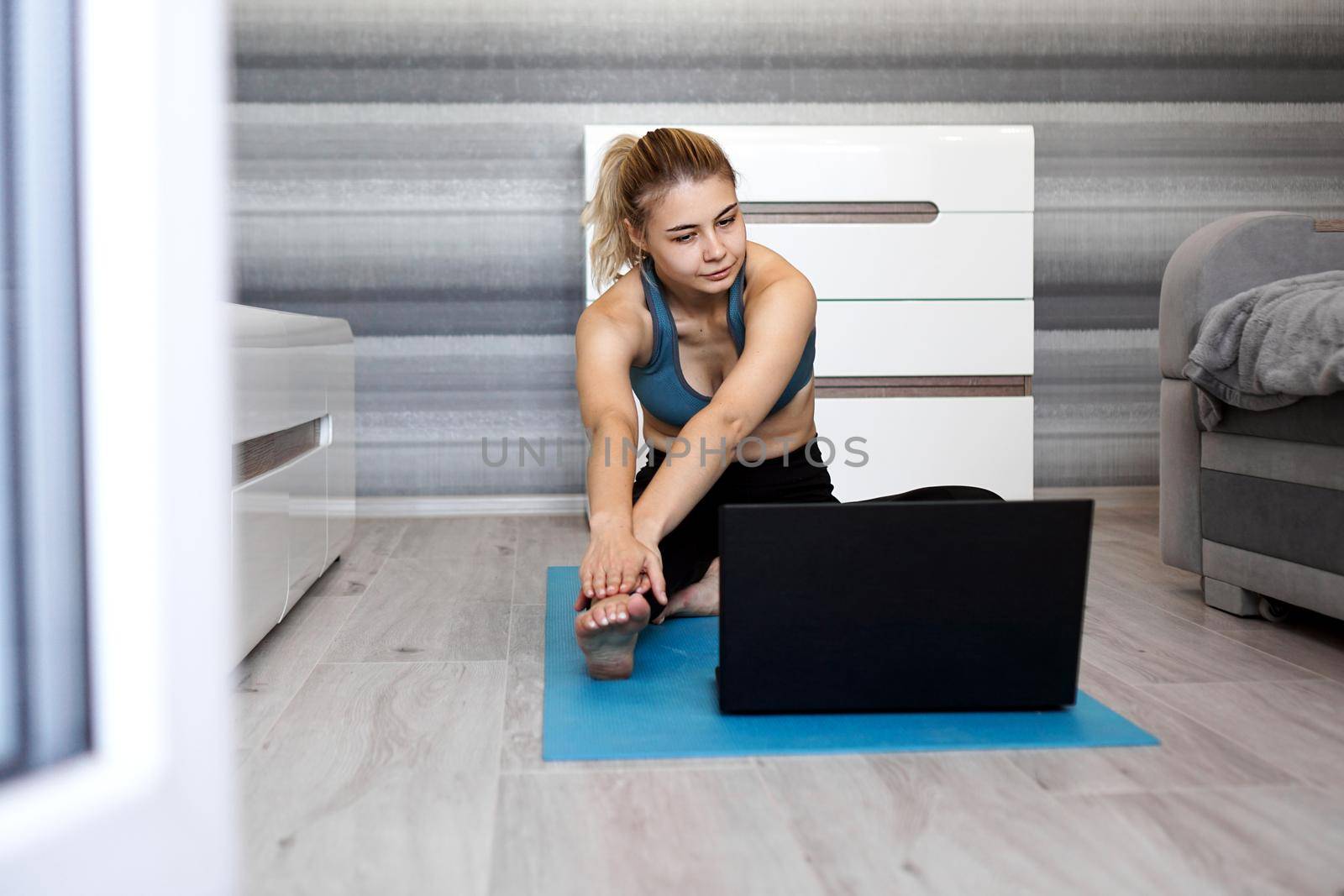 Pretty young woman in sportswear watching online video on laptop and doing exercises at home. Distant training with personal trainer, online education