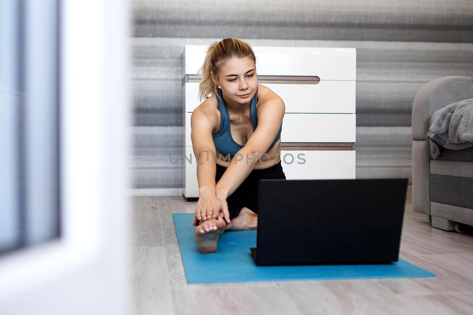 Woman in sportswear watching online video on laptop and doing exercises at home by natali_brill