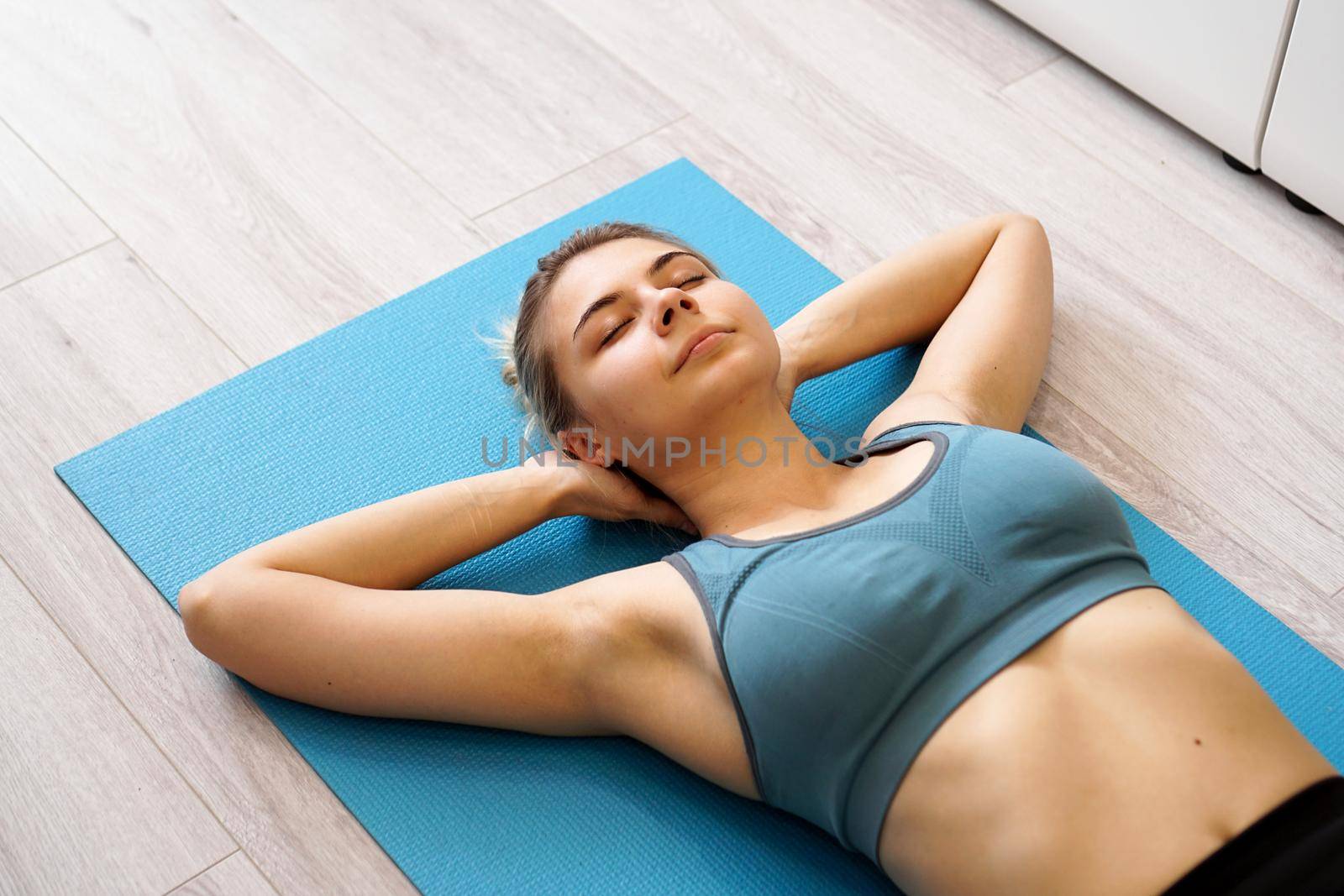 Top view of beautiful young woman lying on yoga mat after workout. Fit female relaxing on floor at home.