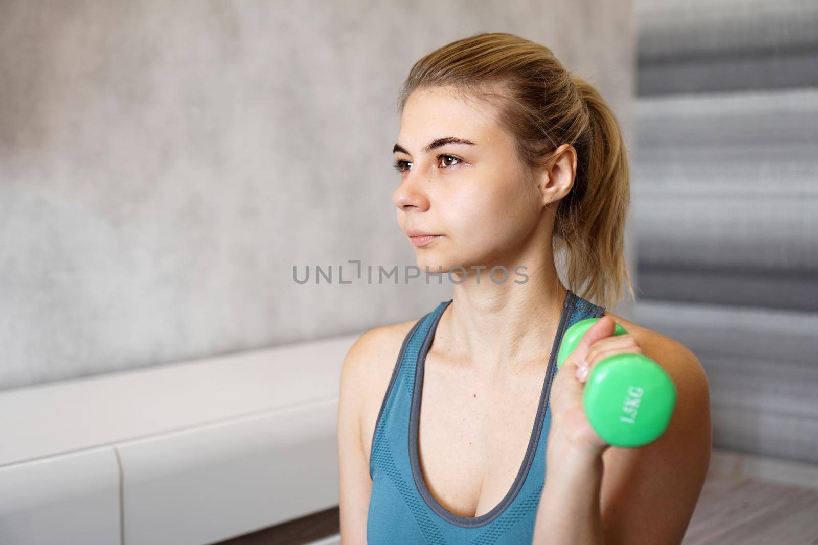 Portrait of a woman who holds a dumbbell in her hands in a bright room at home