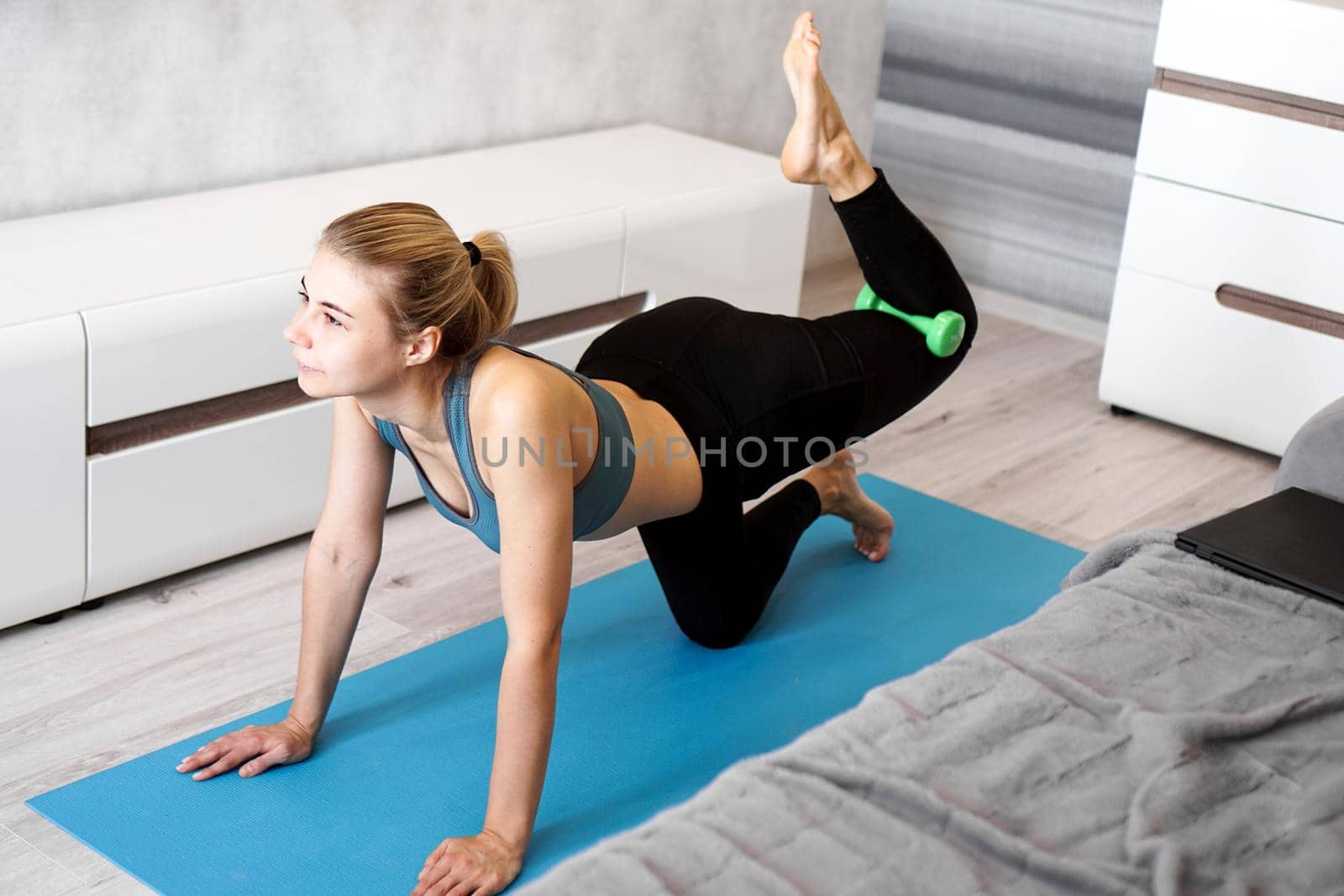 Pretty young trainer doing exercise, using dumbbells. She is training at home, wearing fashionable sport wear