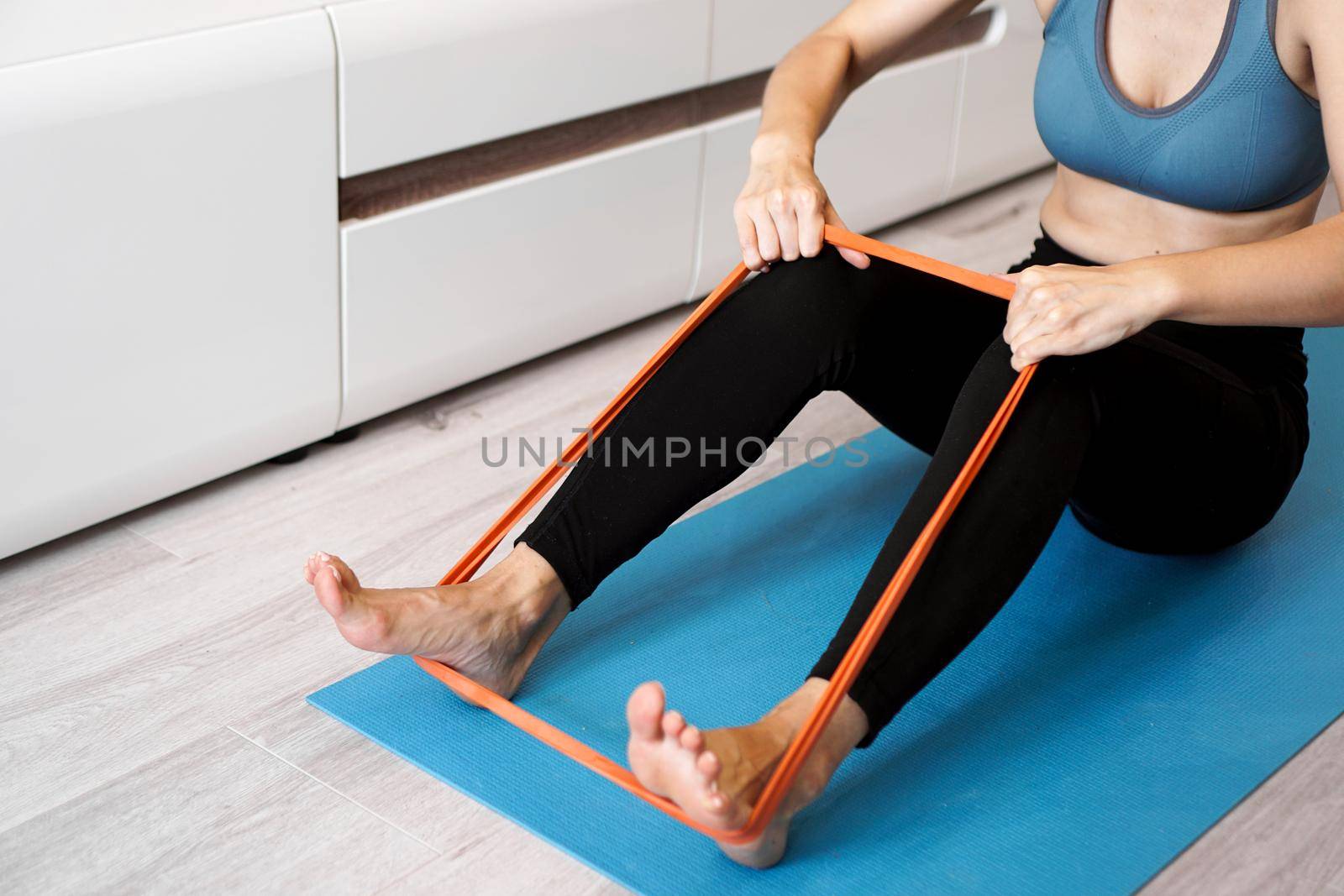 Young woman with elastic band. She trains her legs at home. Healthcare and lifestyle concept