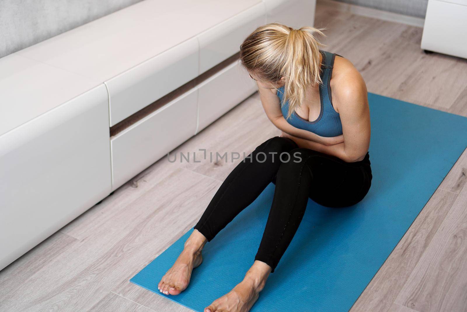 Fitness woman having pain in stomach during home workout by natali_brill