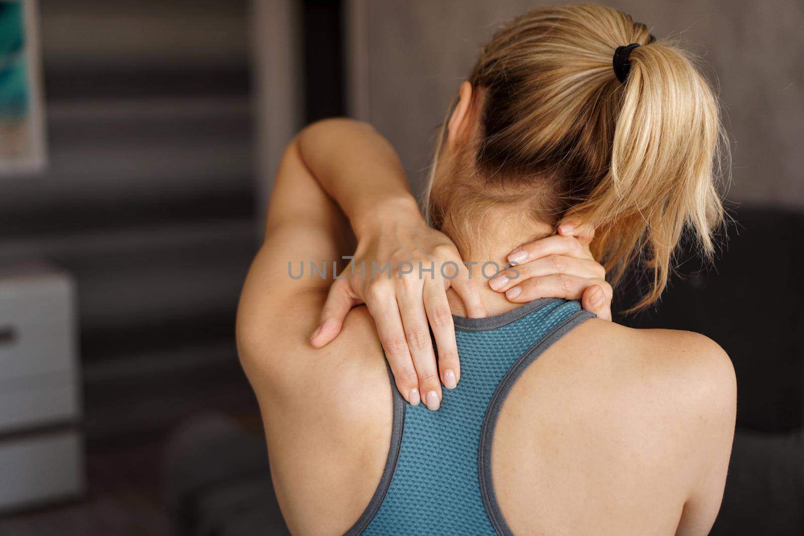 Sports injury concept. Athletic girl feeling pain in her neck against blurred background. Pain after home workout