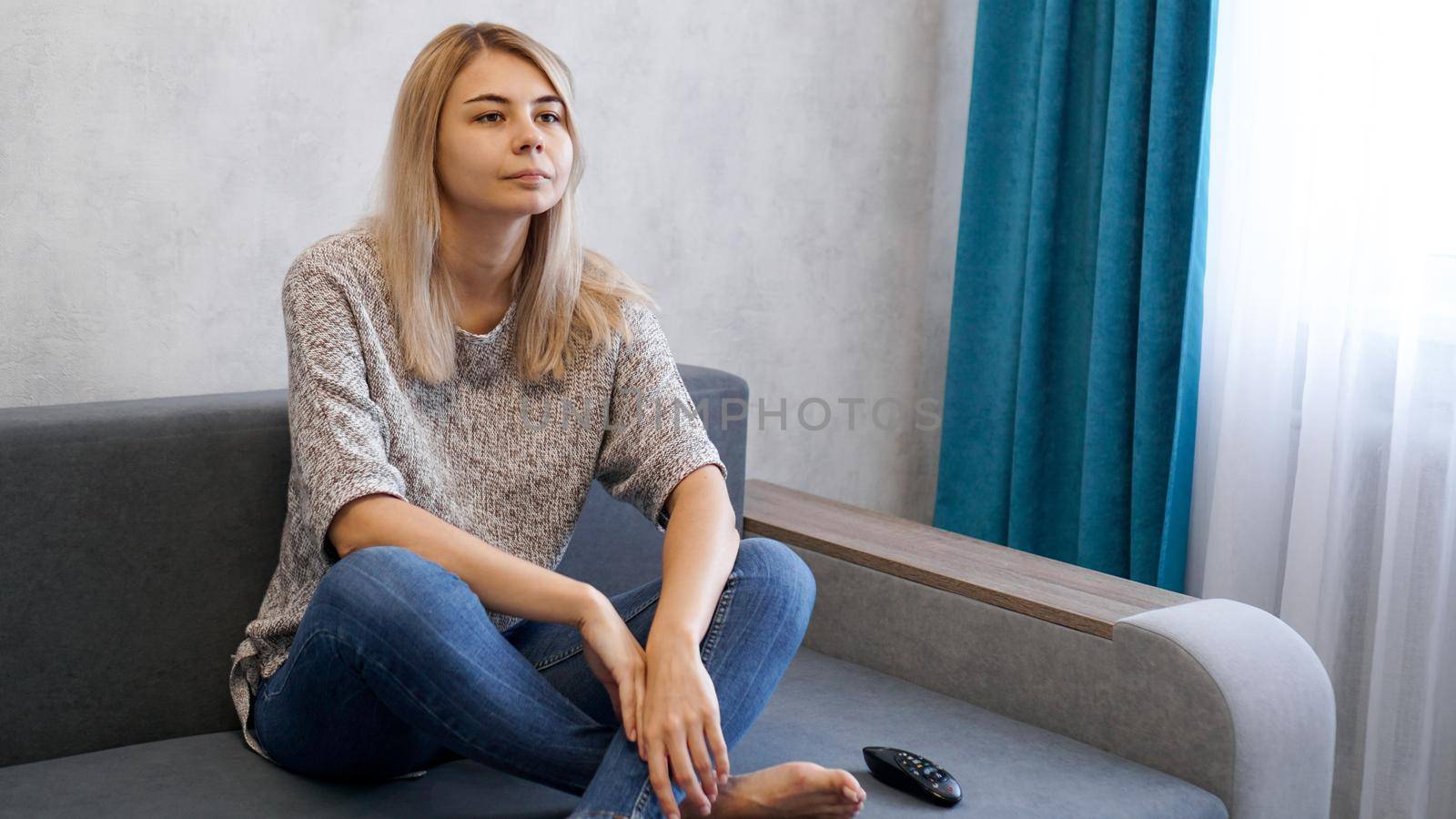 An attractive young woman watching TV on the couch at home, no emotion on the face