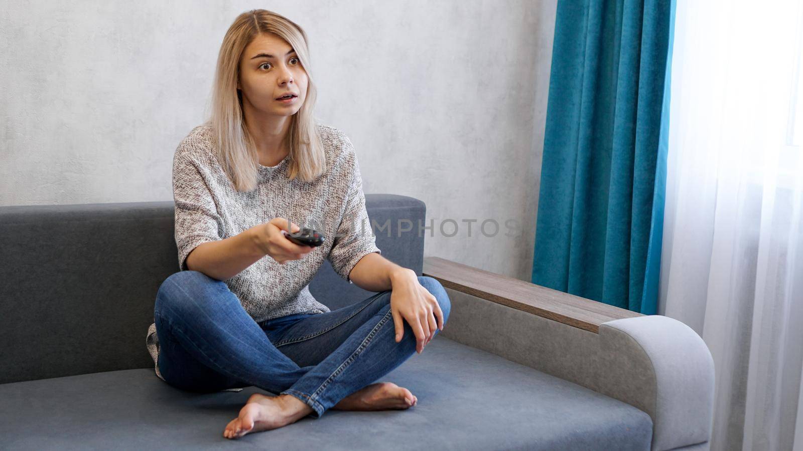 Young beautiful woman watching television on couch at living room surprised and excited