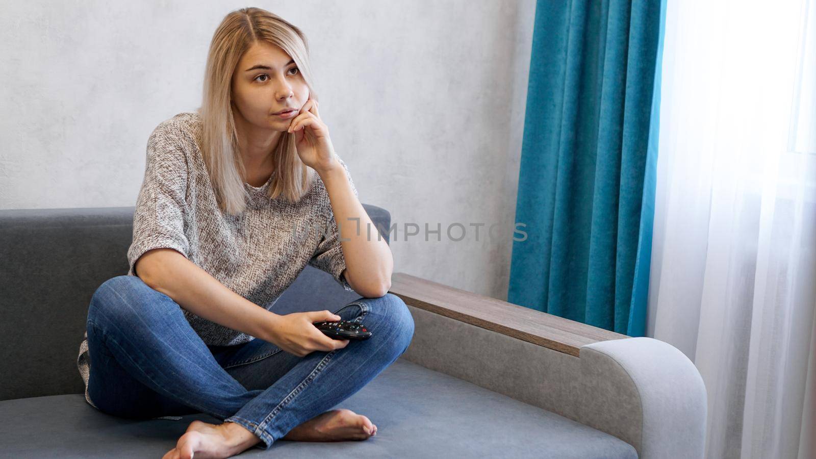 A young bored woman at home watching tv with remote