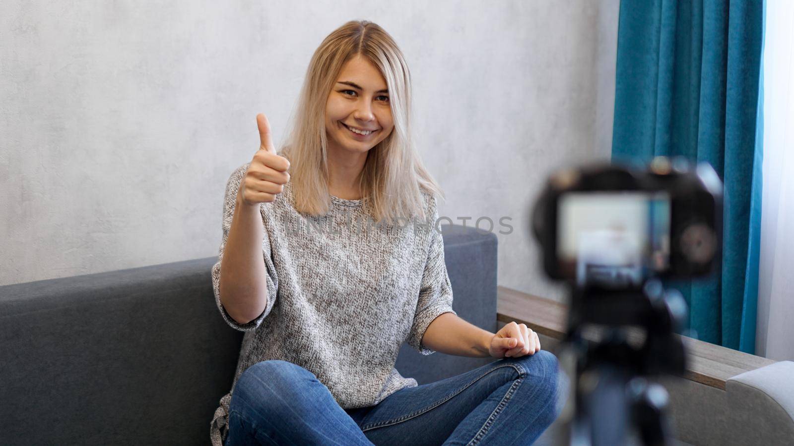 Wwoman or blogger with camera recording video and showing thumbs up at home